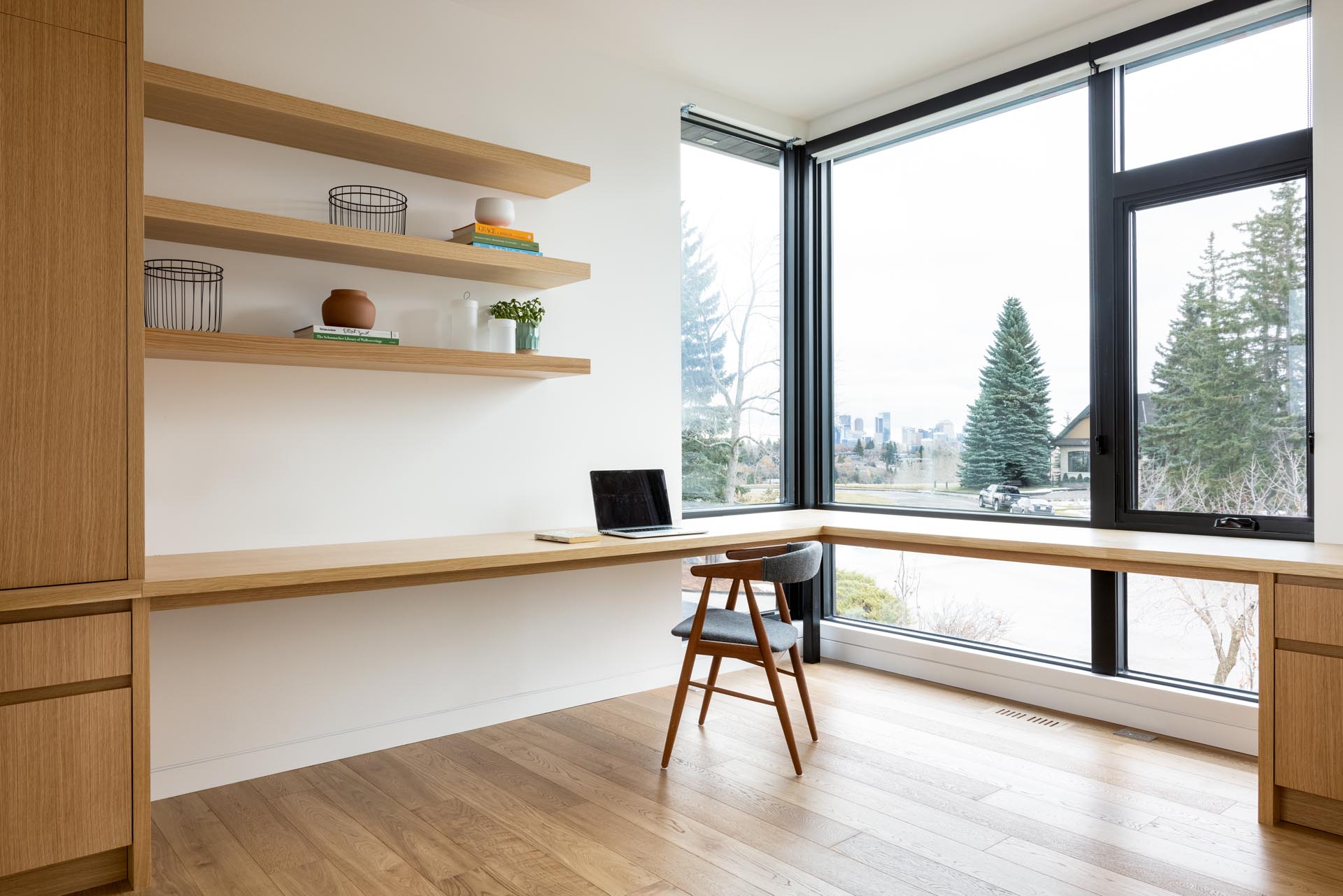 A home office with a custom designed wood desk that wraps around the corner of the room. Open shelving and cabinets add additional storage to the room.