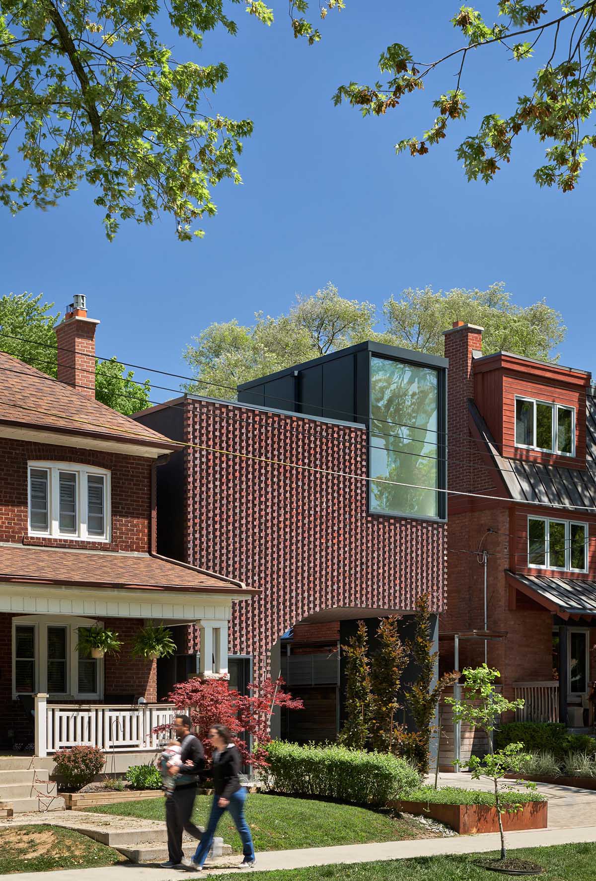 The brickwork that covers the facade and wraps the ceiling and walls of the carport of this modern house plays into Toronto’s history of masonry detailing.