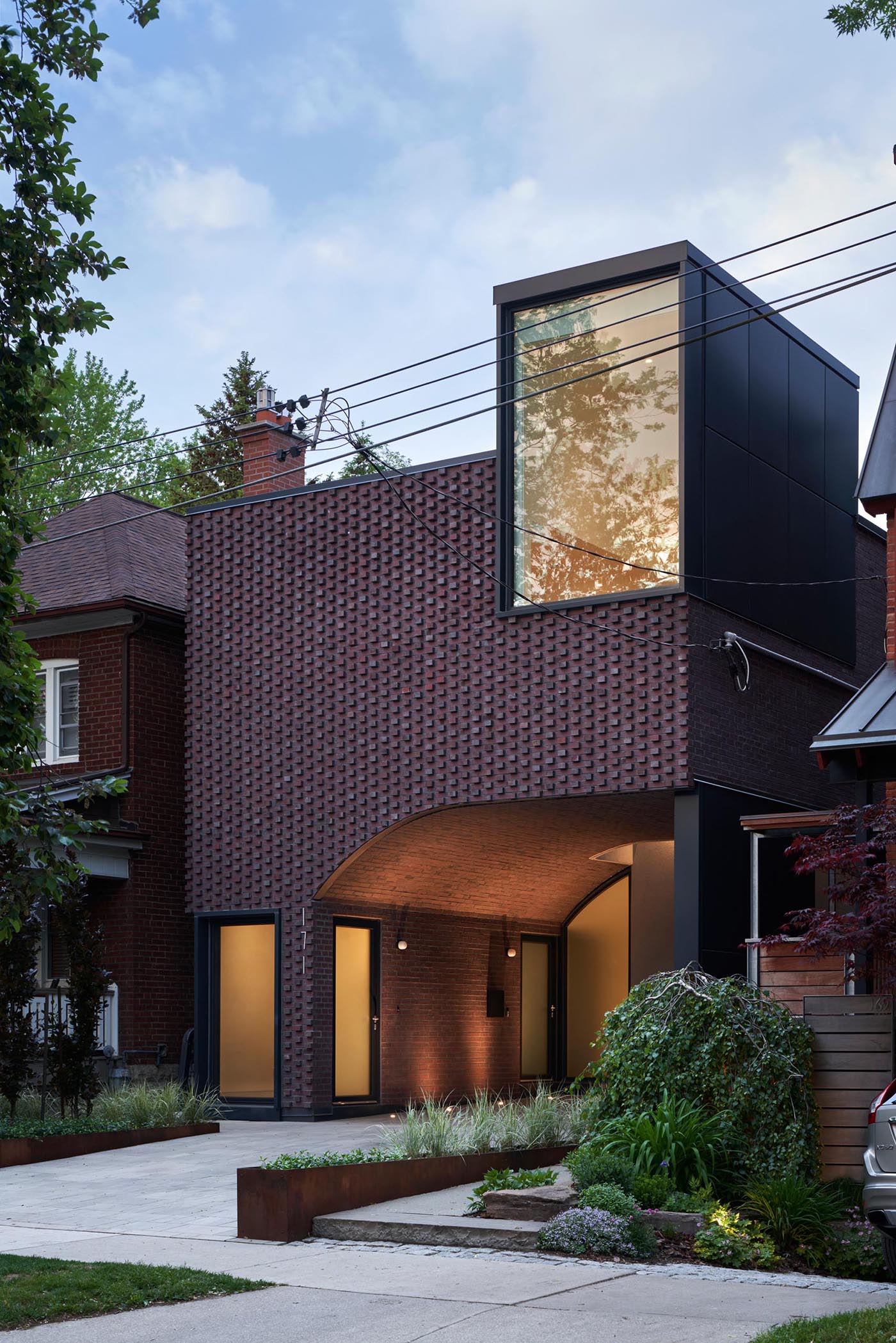 At dusk, the lights from the interior of the home and the featured exterior lighting highlight the windows and doors, and create a soft ambient glow.