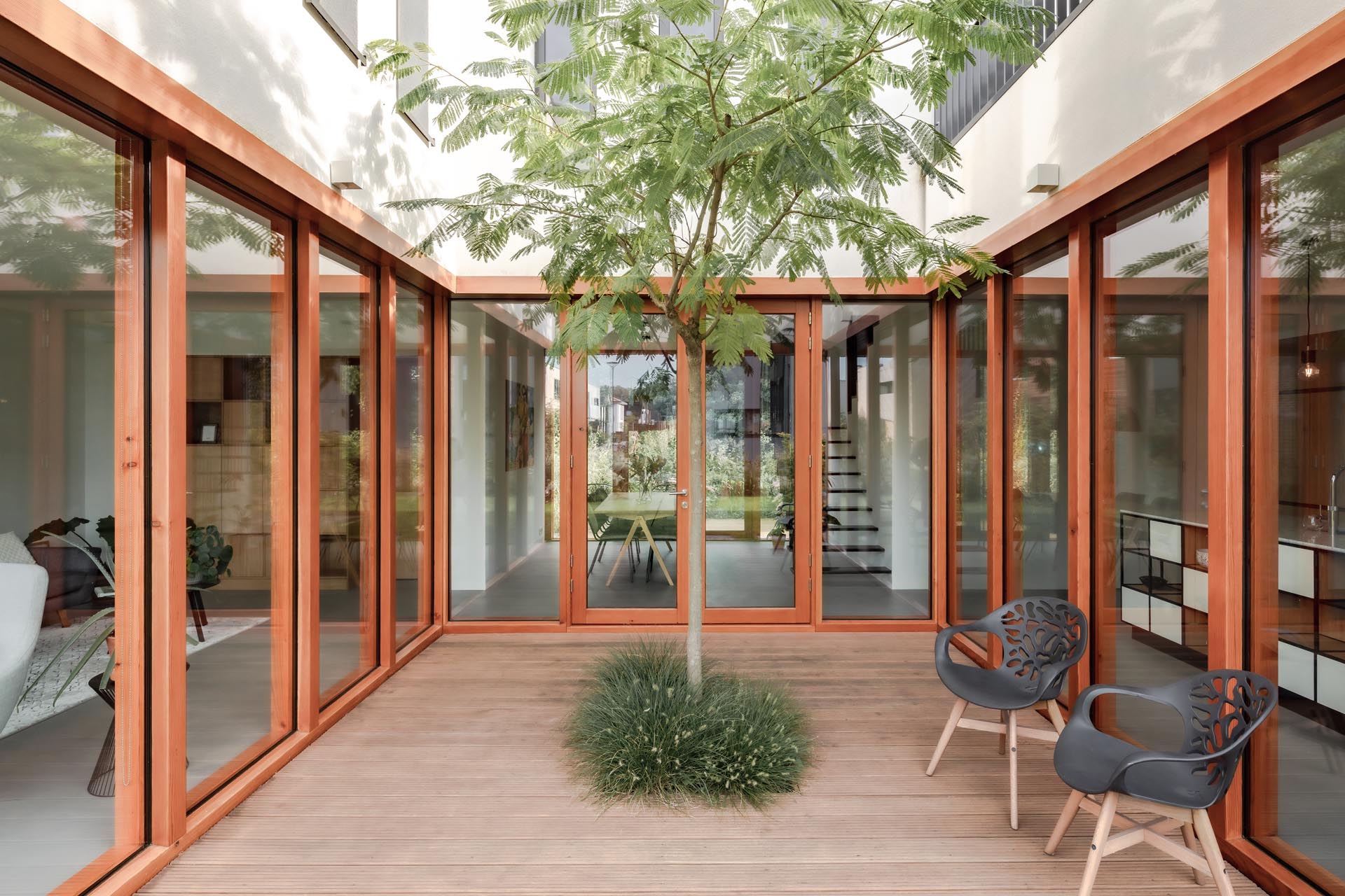 A modern home with windows and glass doors that wrap around a courtyard with a tall tree and wood deck.