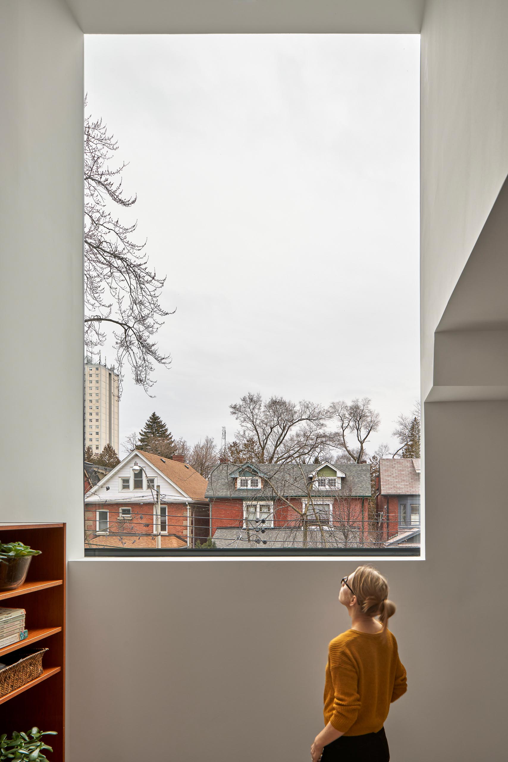 On the upper floor of this modern home, there's a large window that frames the neighborhood.