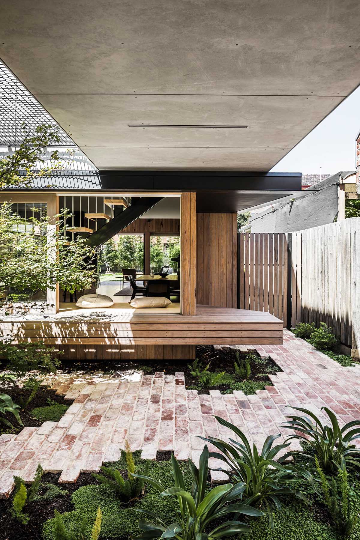 Connecting the interior spaces with the carport of this modern home, is a small courtyard with bricks surrounding small pockets of greenery. In the open space above, there's a net for relaxing in the sun.