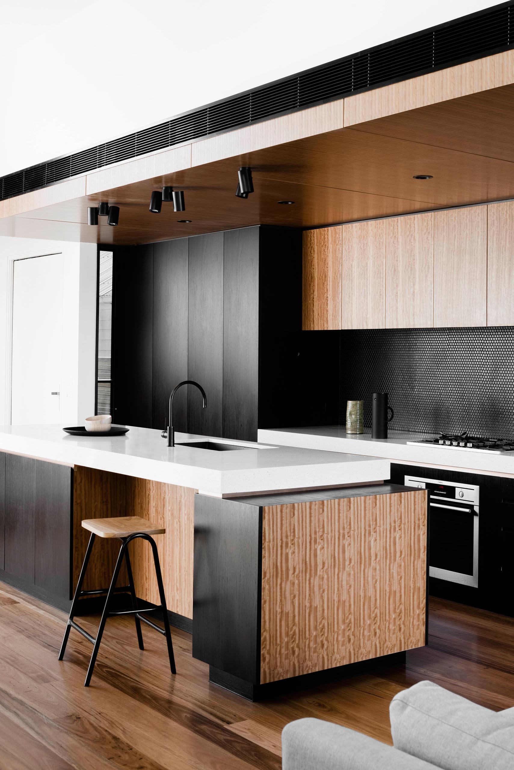 A modern kitchen with black and wood cabinets, a penny tile backsplash, and a white countertop.