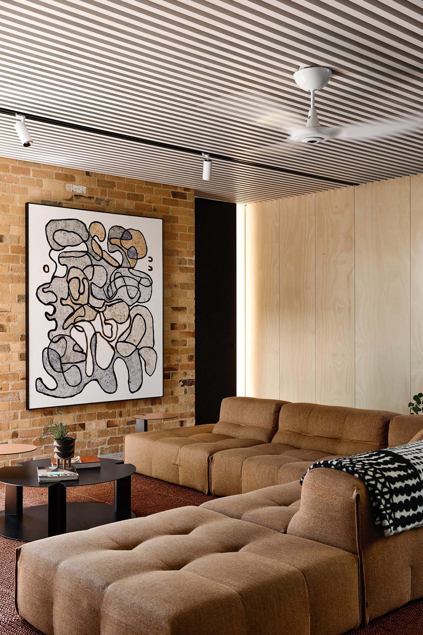 Inside this modern home, the living room is furnished with a large sofa and abstract artwork, while a white slat ceiling adds a unique design element.