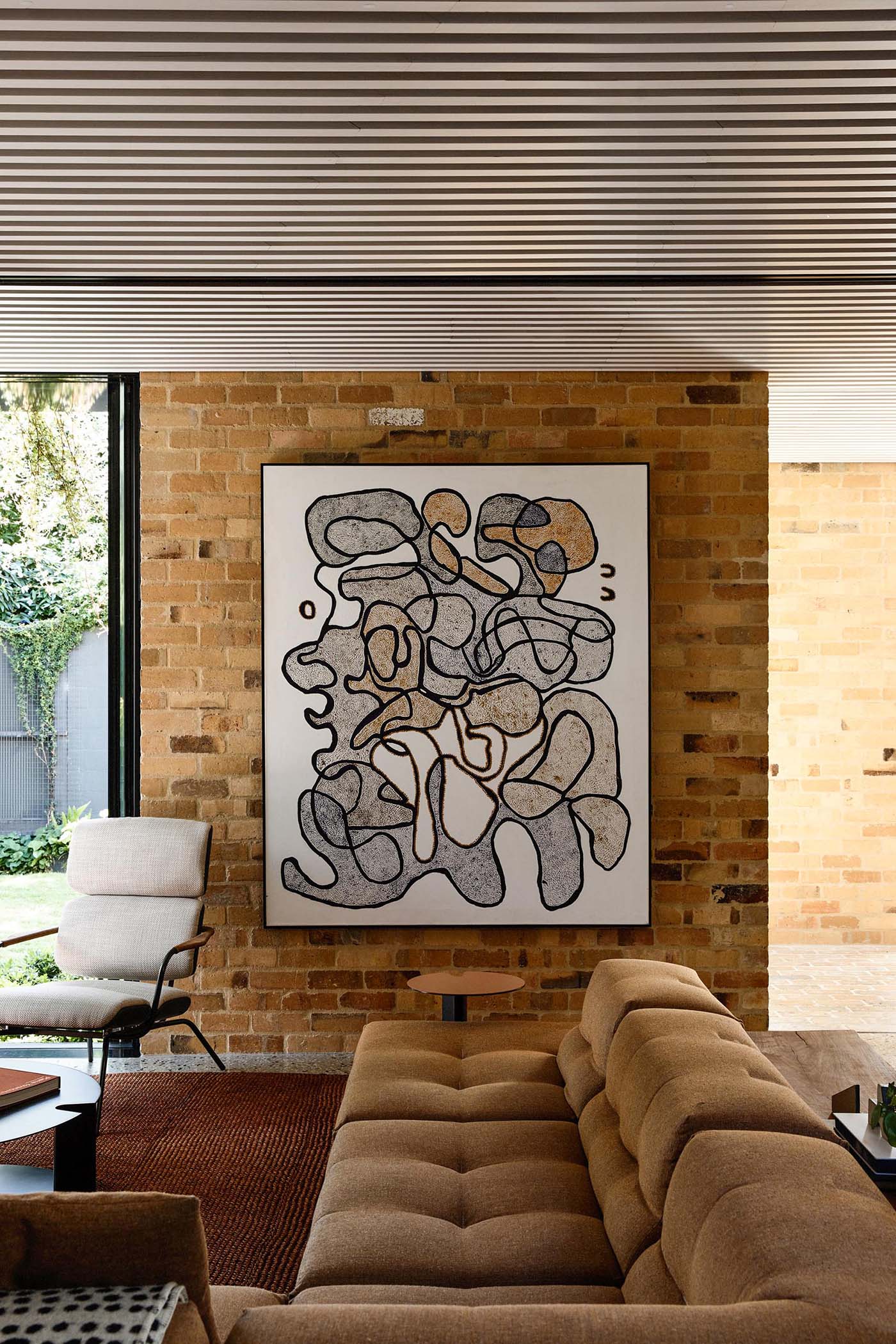 Inside this modern home, the living room is furnished with a large sofa and abstract artwork, while a white slat ceiling adds a unique design element.