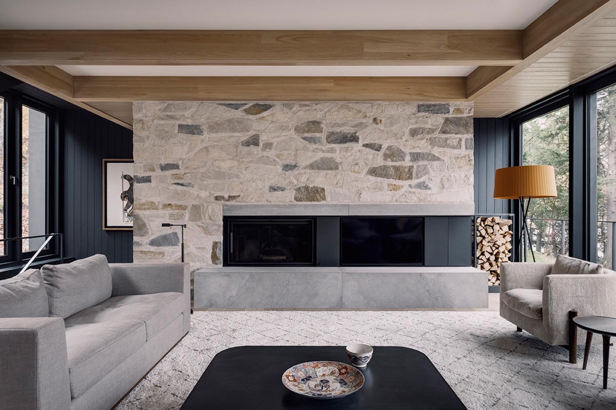 In this modern living room, there's wood accents on the ceiling, while the black fireplace is positioned within a stone wall.