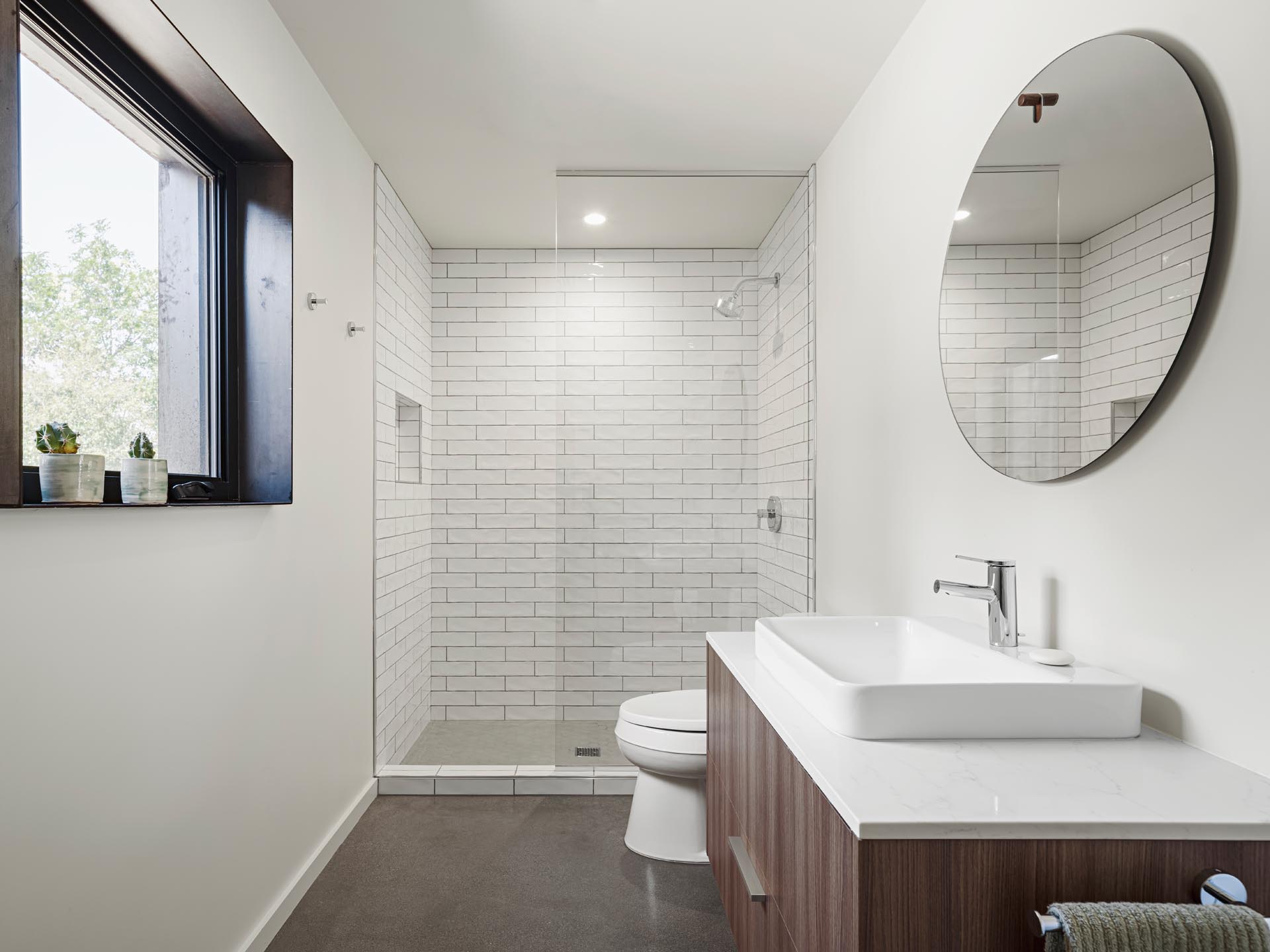 A modern white bathroom with a wood vanity and white rectangular tiles.