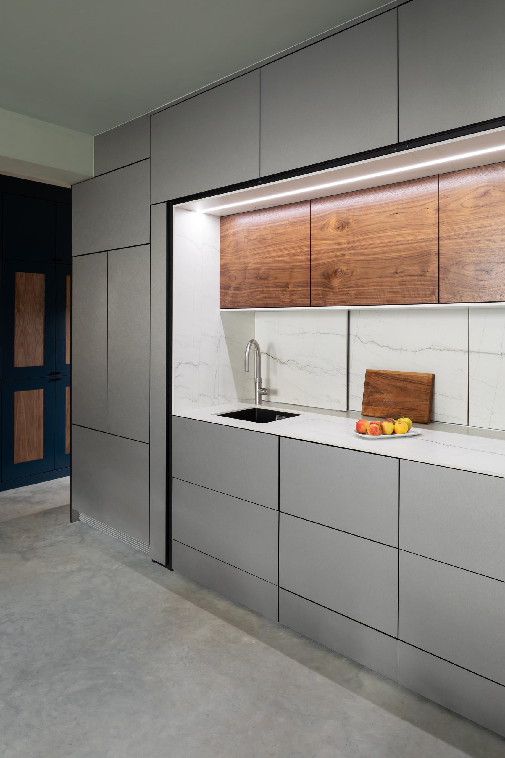 The main section of this modern kitchen includes a small sink, a cooktop, counter space, hidden lighting, drawers with minimalist fronts, and wood upper cabinets.