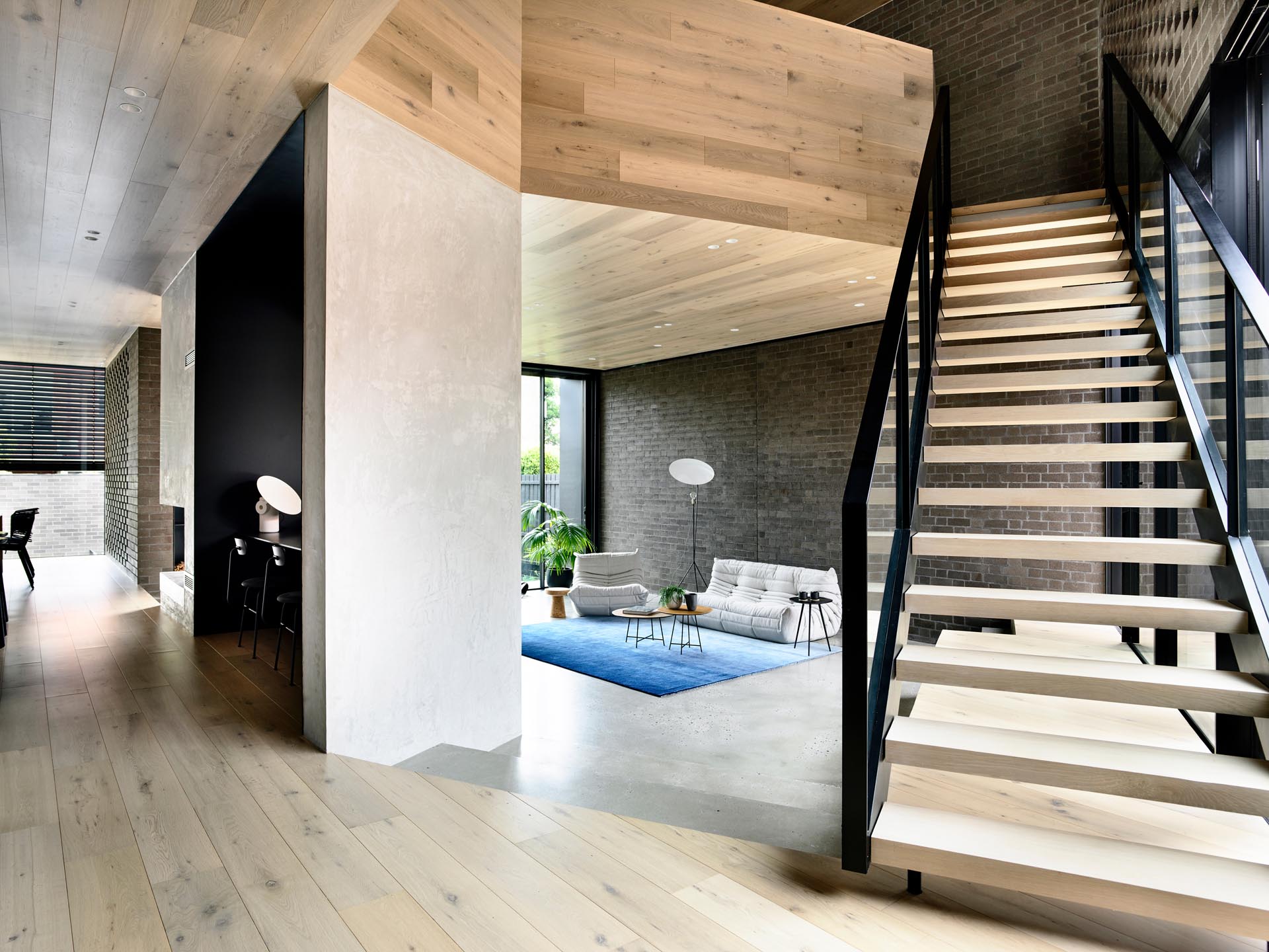 A modern sculptural wood, steel, and glass staircase which is set under a folding origami, timber-lined ceiling.