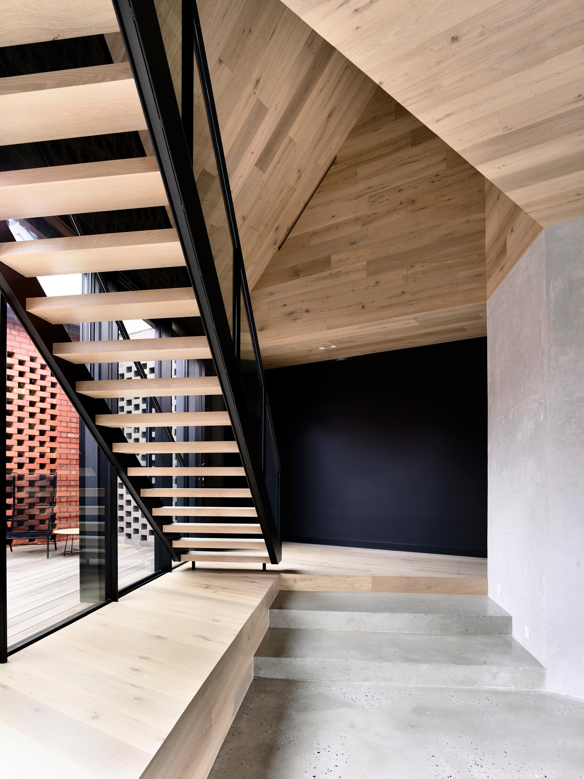 A modern sculptural wood, steel, and glass staircase which is set under a folding origami, timber-lined ceiling.