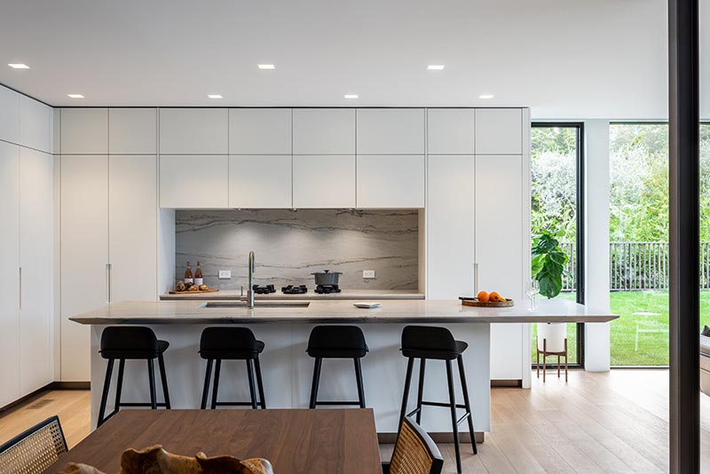 A modern kitchen designed with floor-to-ceiling minimalist white cabinets, and an island with a cantilevered countertop.