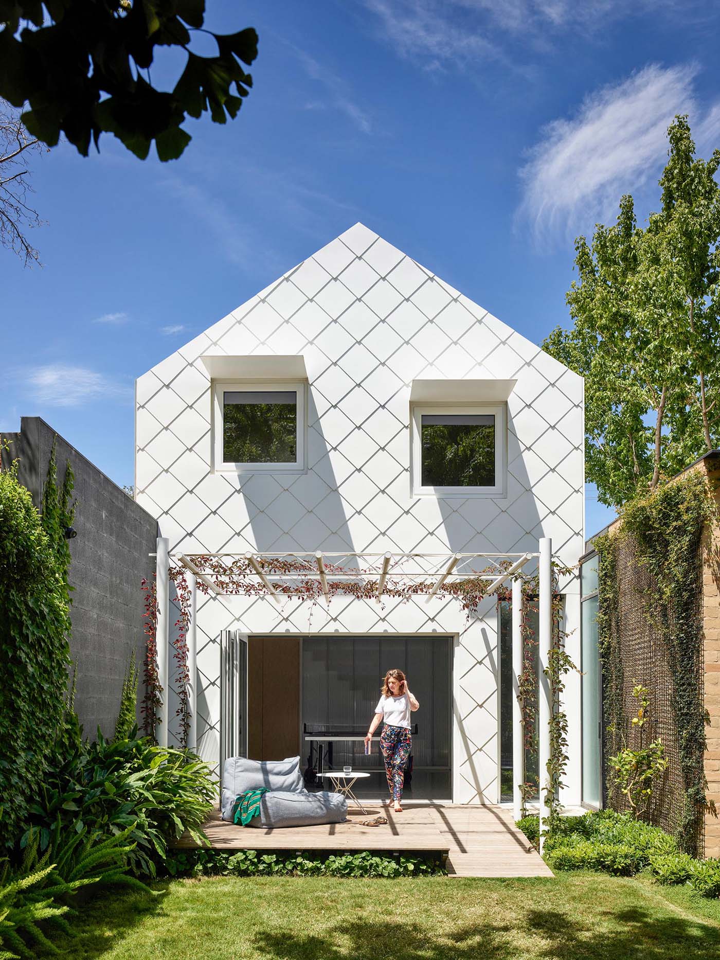 The exterior of this modern home looks like a pretty, white shingled cottage with a perfect pitched roof.