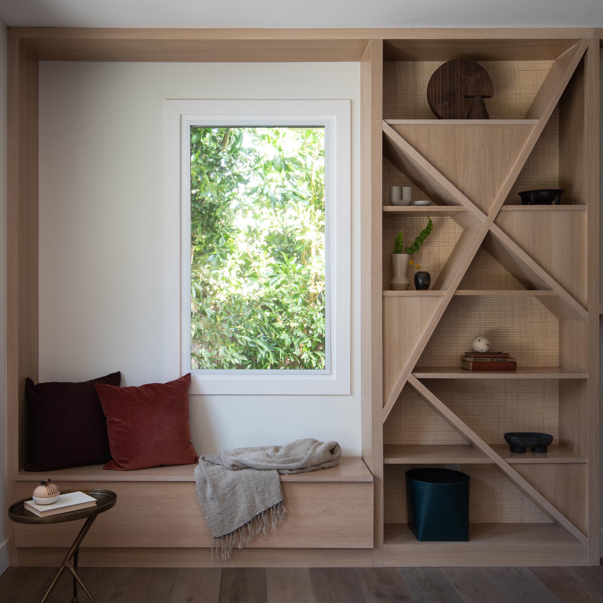 A modern shelving unit with a natural cane backing has been installed next to a window seat.