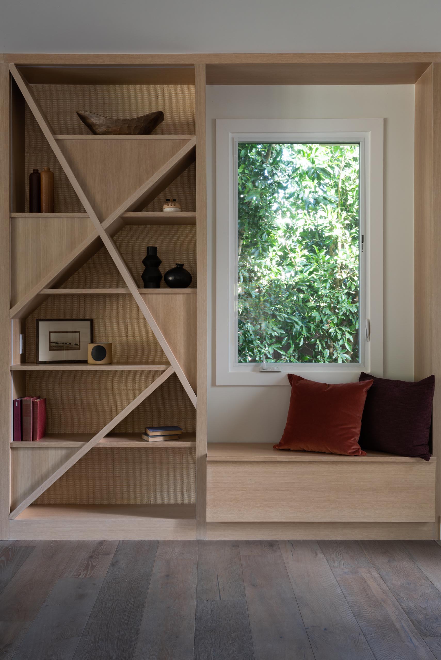 A modern shelving unit with a natural cane backing has been installed next to a window seat.