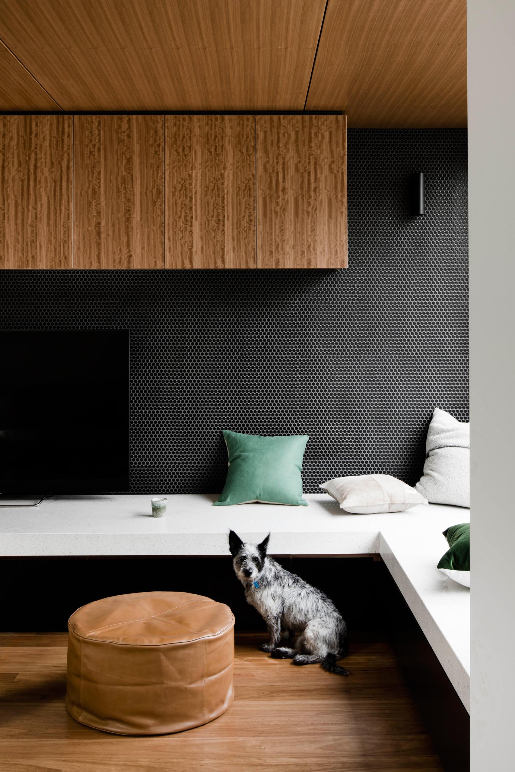 A modern built-in tv stand with a black penny tile backdrop, transforms into a daybed by a window.