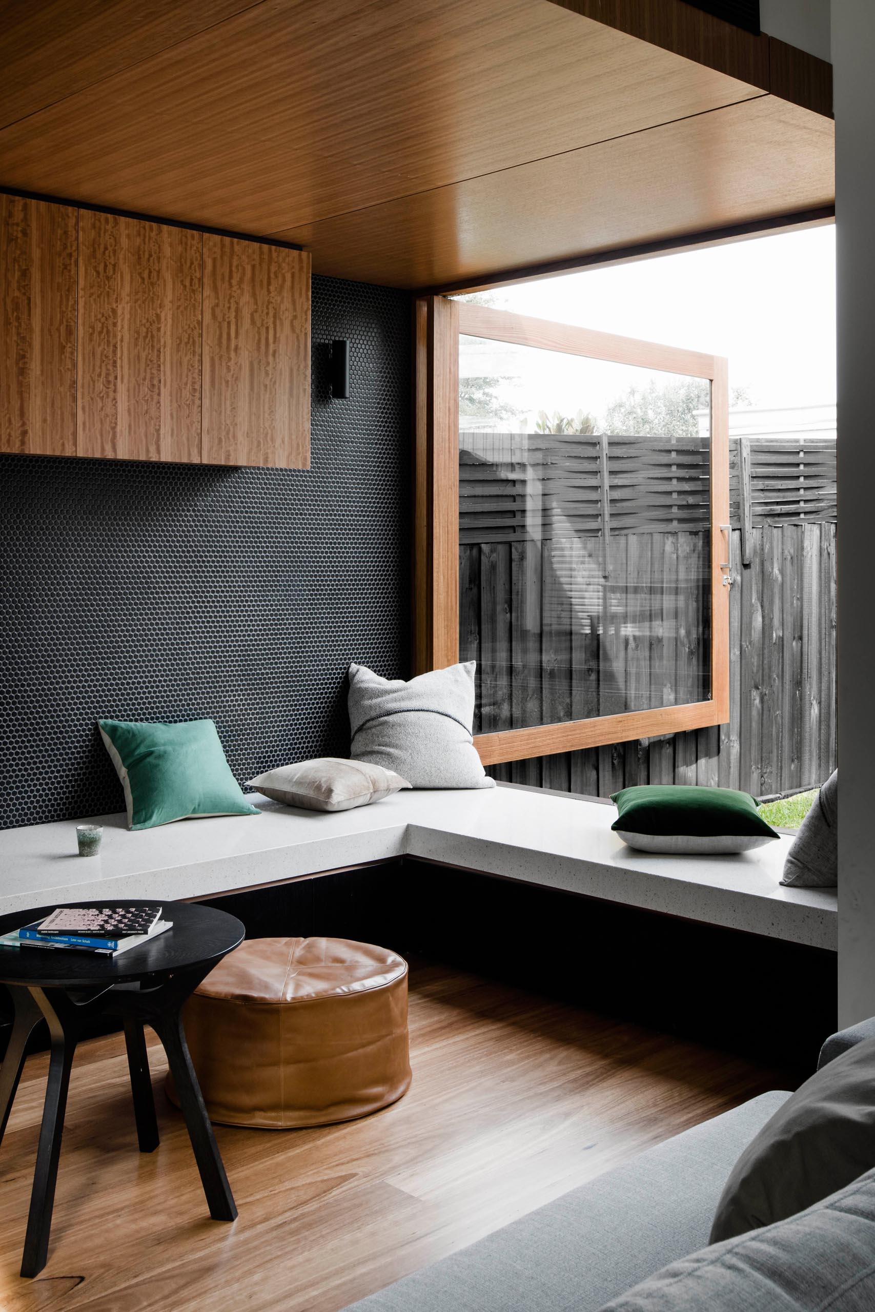 A modern kitchen with black cabinets and wood accents, has a white countertop that transforms into a desk, TV stand, and window bench.