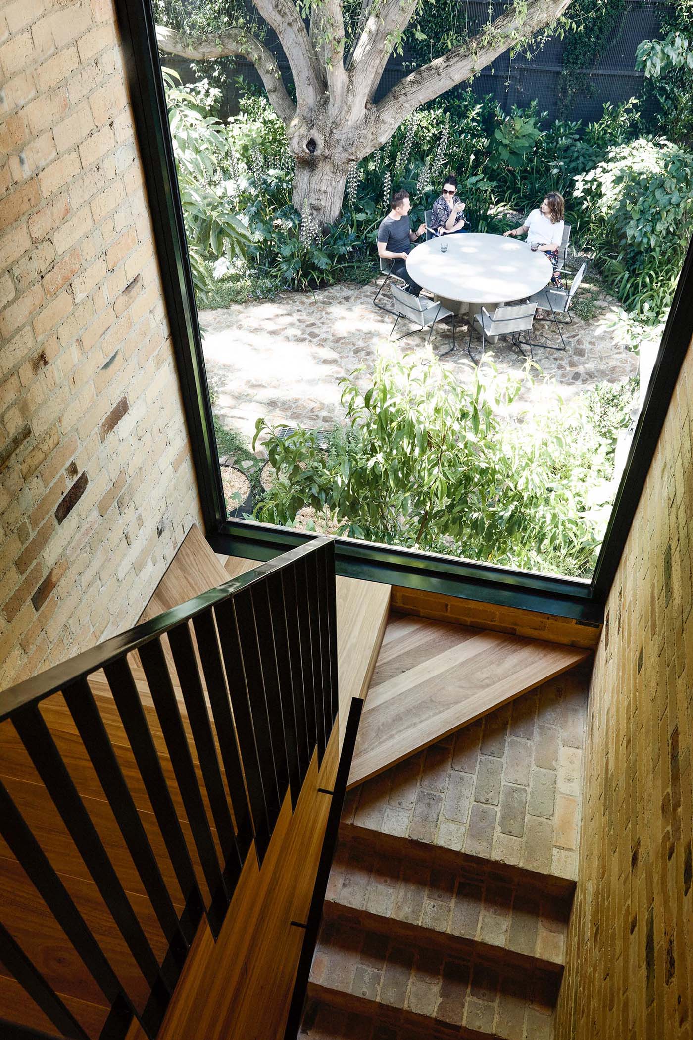 This staircase features the recycled yellow bricks that then transition to connect with the wood stair treads. A large black framed window perfectly frames the tree and outdoor dining area.