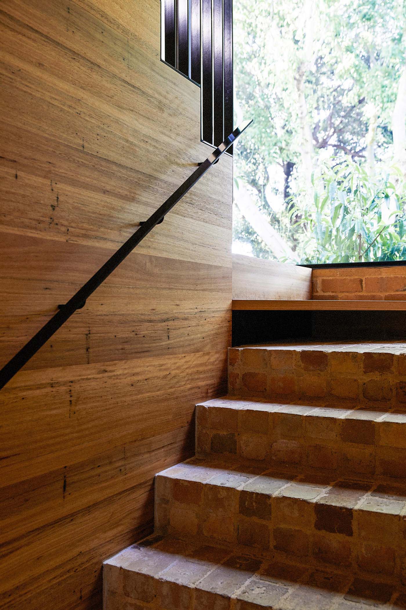 This staircase features the recycled yellow bricks that then transition to connect with the wood stair treads. A large black framed window perfectly frames the tree and outdoor dining area.