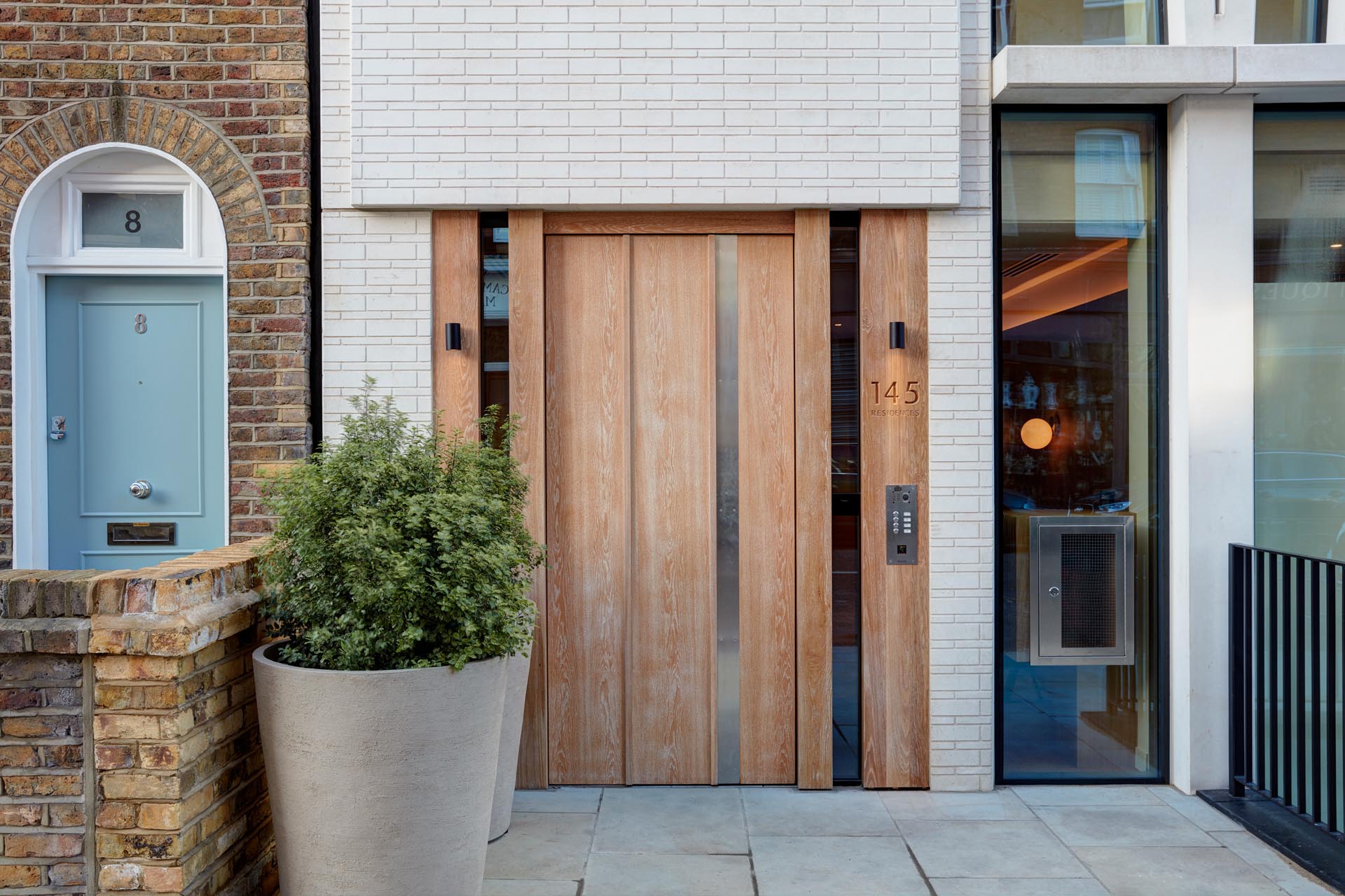 A wood front door surrounded by white brick welcomes people to the building.