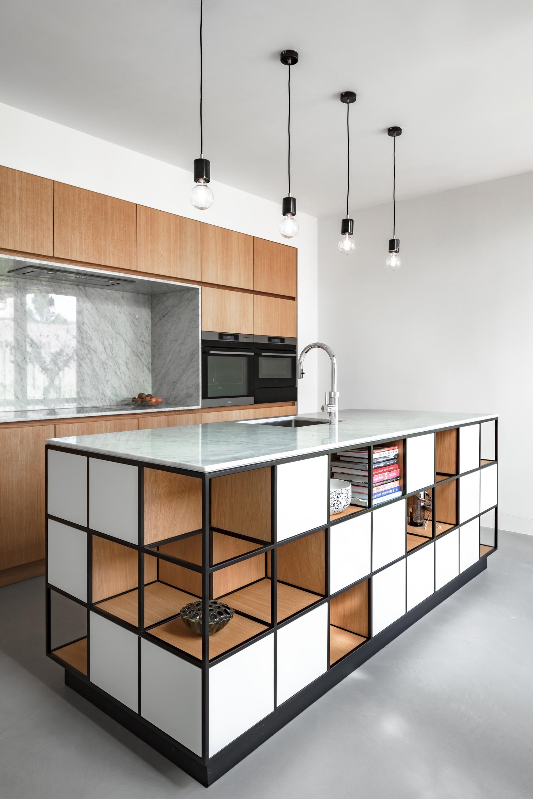 In this modern kitchen, hardware-free wood cabinets line the wall, and an island includes a cube like design with shelving.