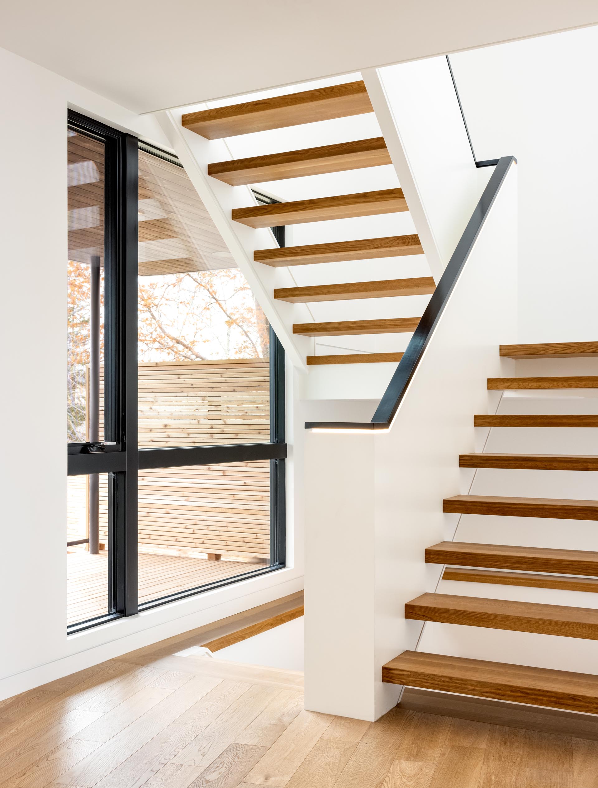 A staircase with wood treads and a black handrail with hidden LED lighting connects to the upper floor of the home.