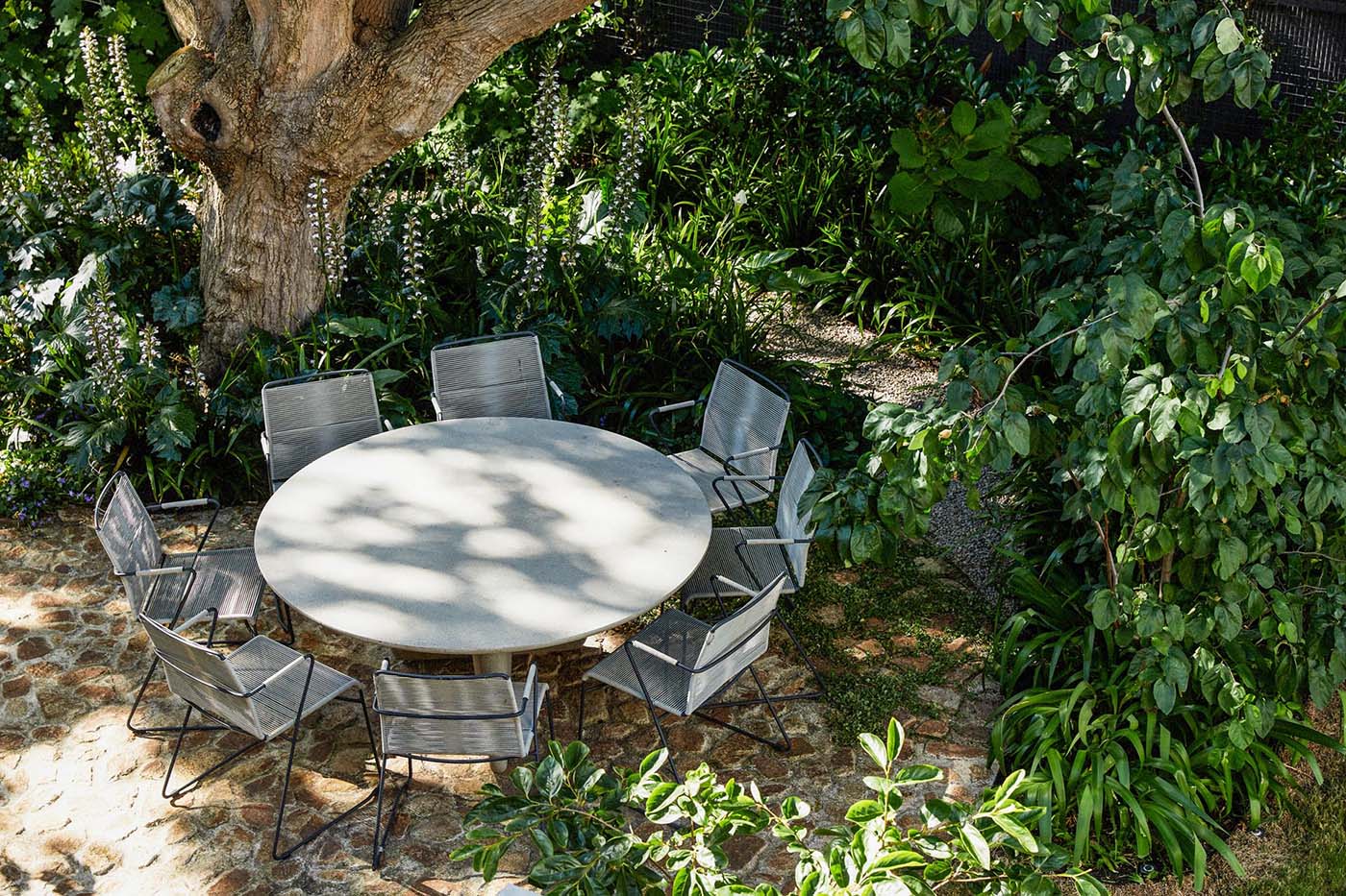 A garden with a round table and stone patio.