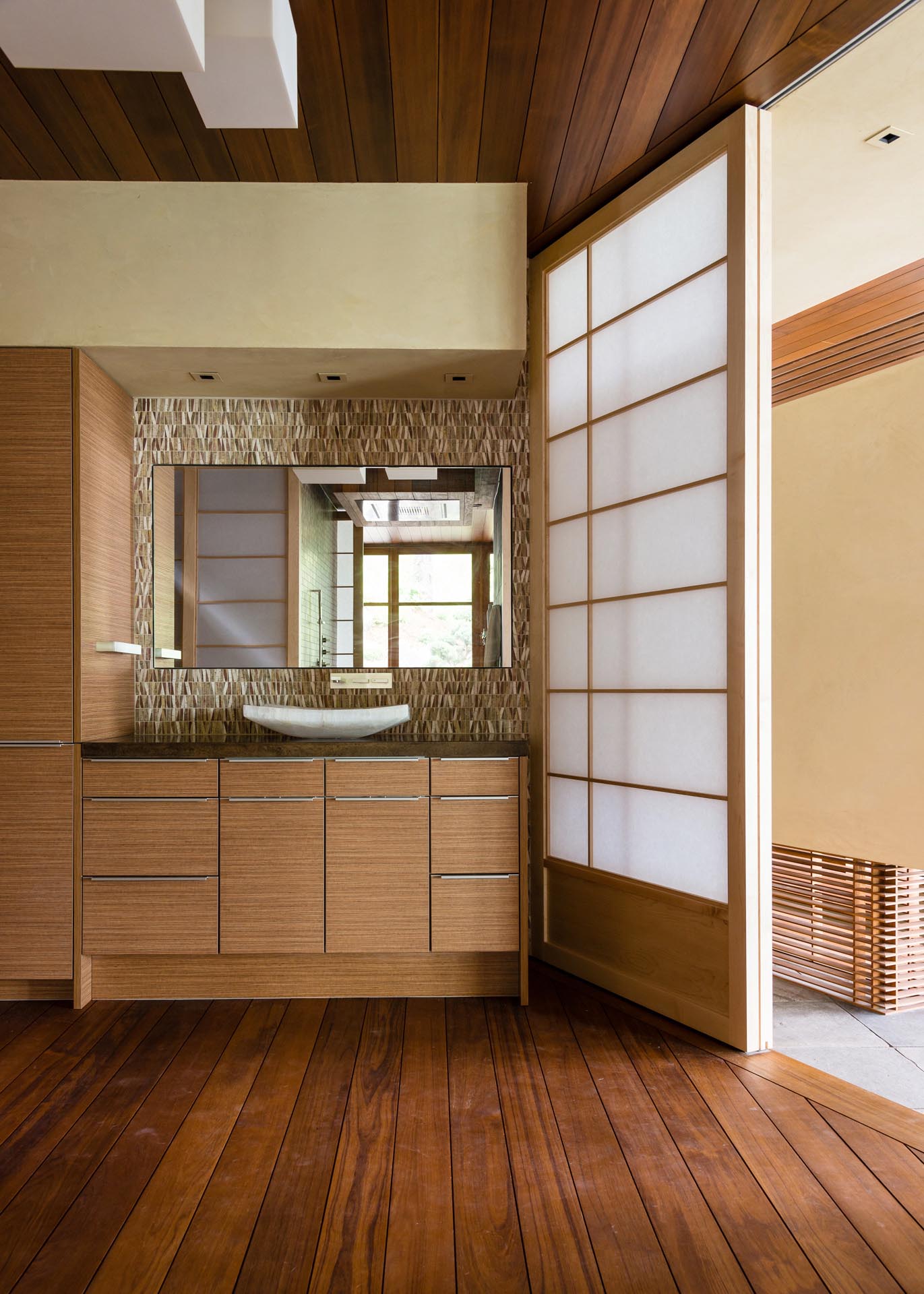 In this bathroom, decorative natural with earthy colors provides a backdrop for the mirror, while a sliding screen door lets the light from the nearby window travel through to the interior space.