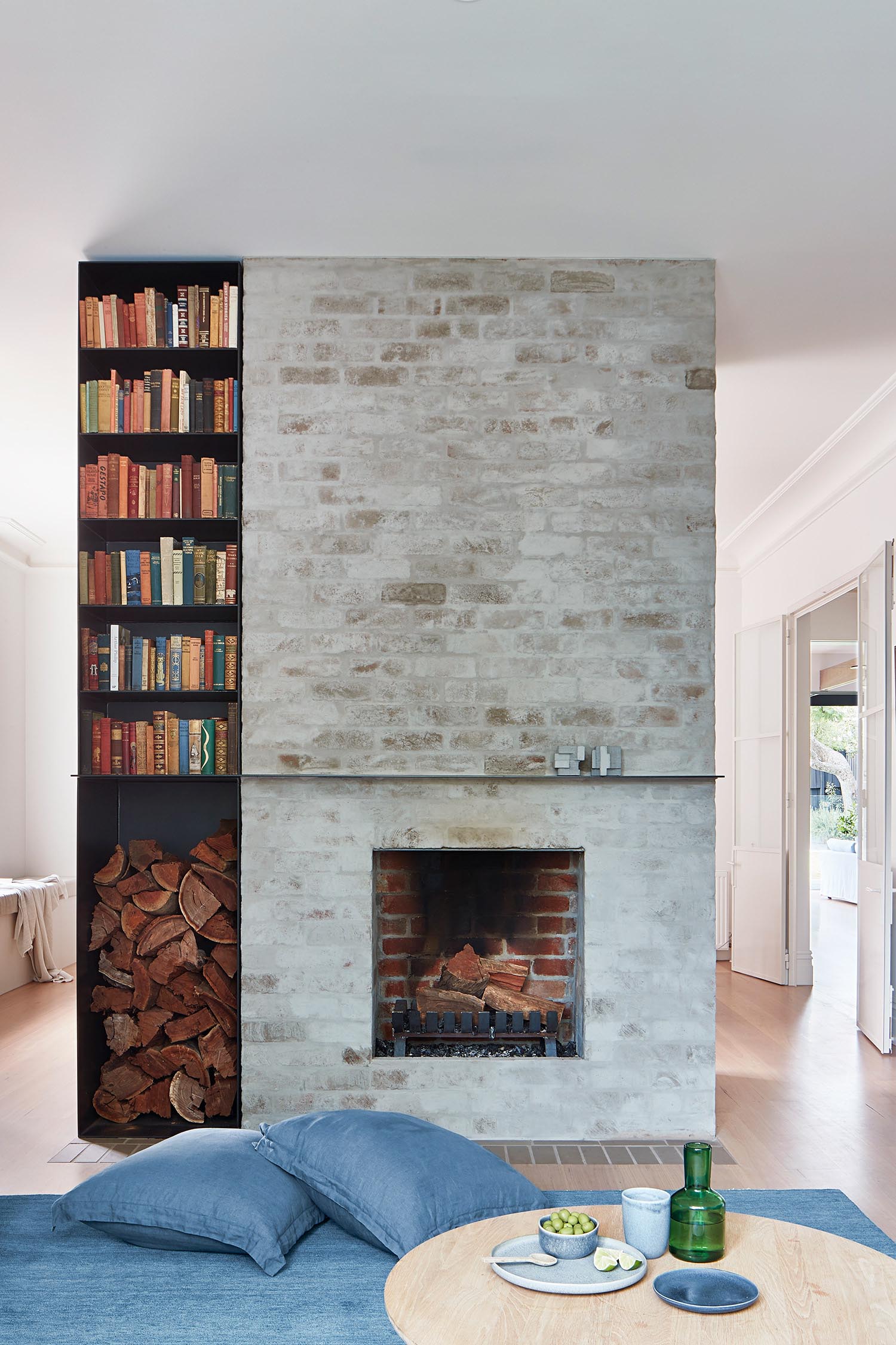 A brick fireplace with firewood storage and a bookshelf.