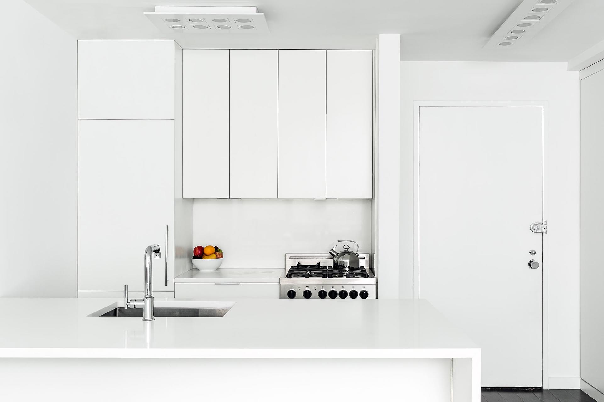 A modern small white kitchen with an integrated fridge and hardware free cabinets.
