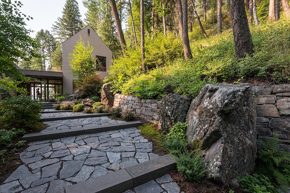 A stone pathway through the trees and shrubs leads to a small collection of stucco-clad buildings perched on a steep slope high above Whitefish Lake.