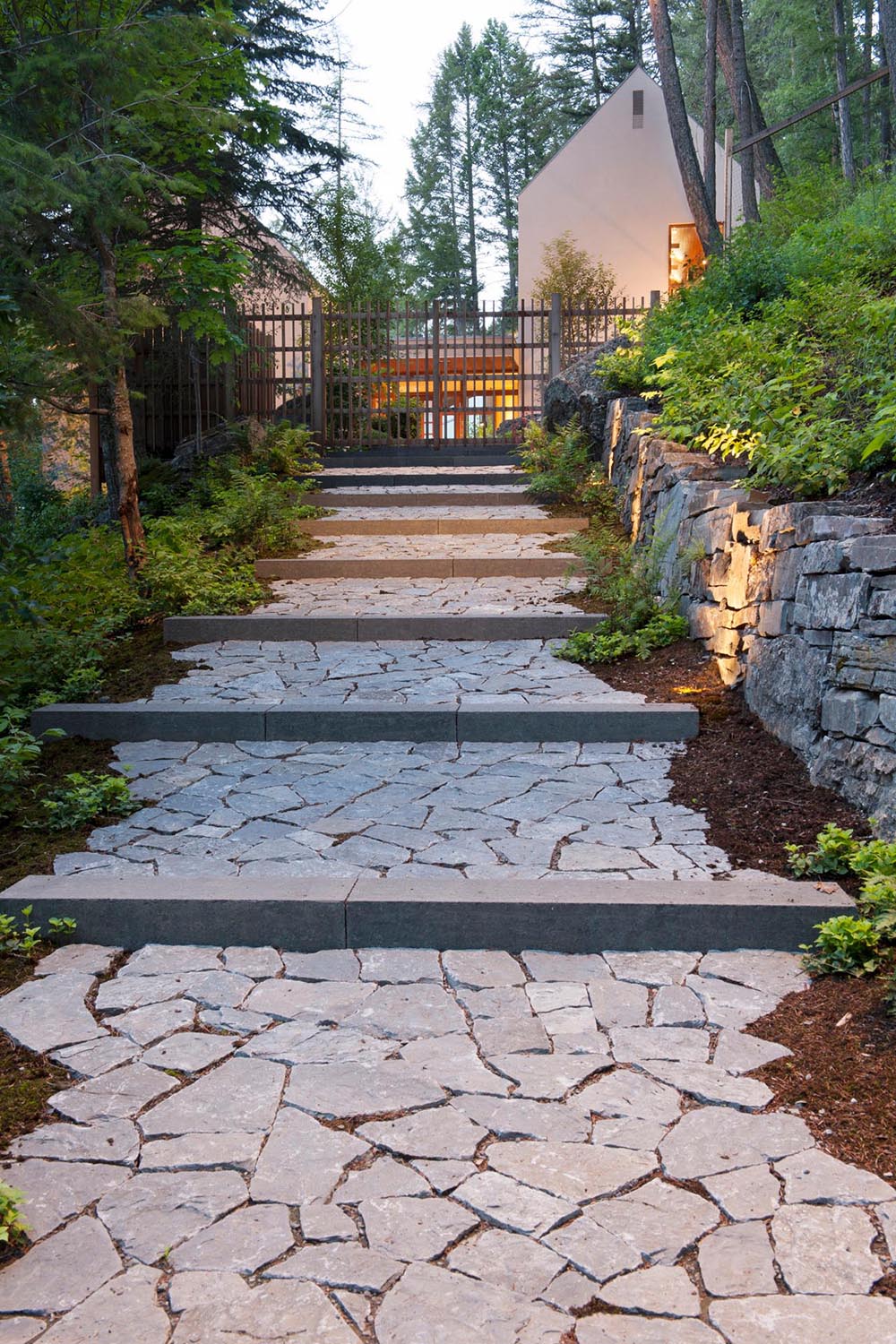 A stone pathway through the trees and shrubs leads to a small collection of stucco-clad buildings perched on a steep slope high above Whitefish Lake.