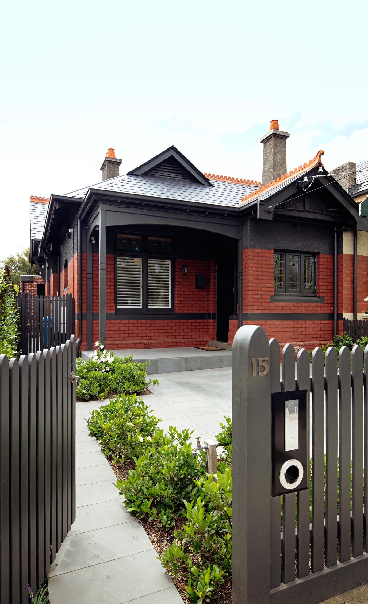 An Australian home with dark grey trim and red bricks.