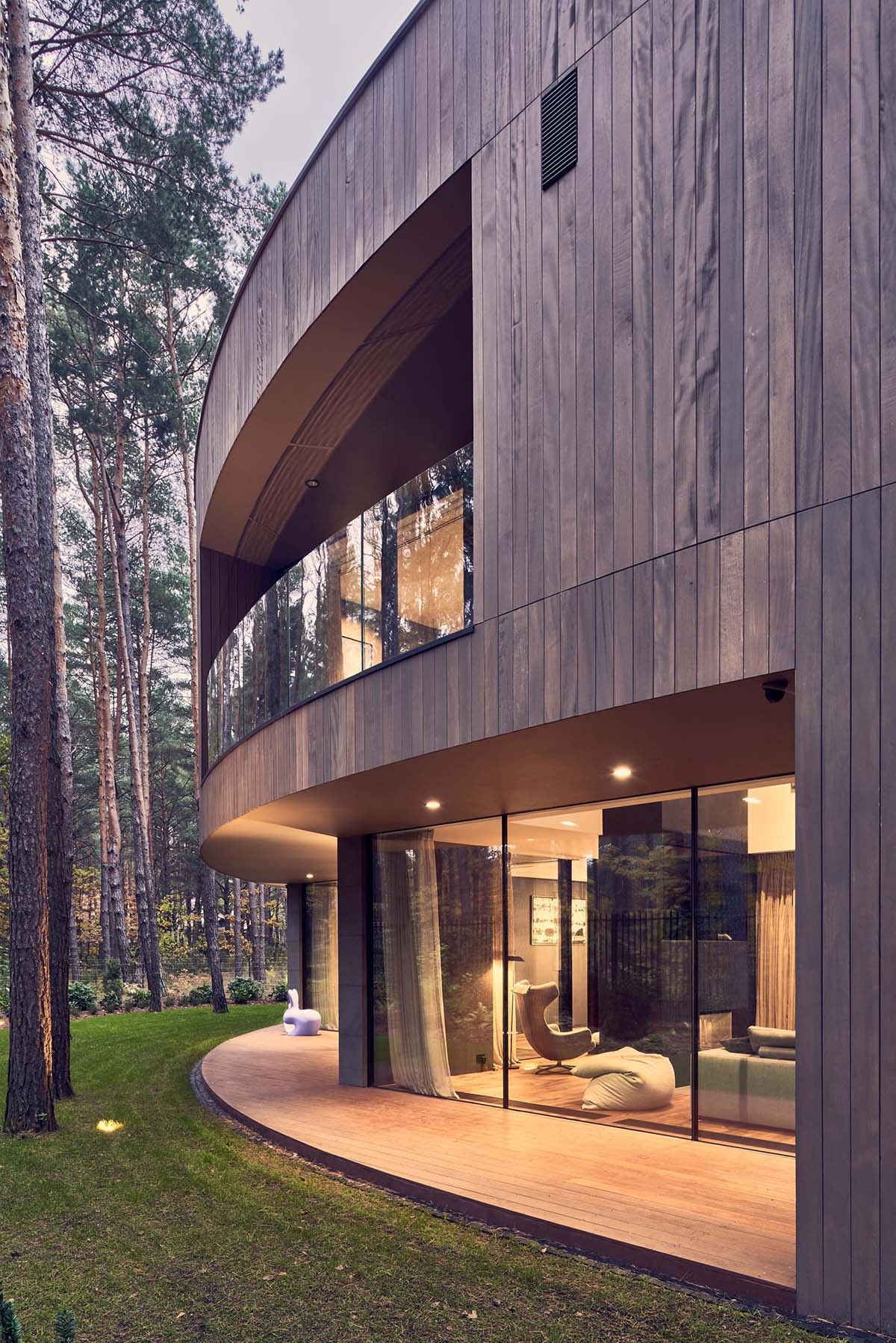 A modern circular home with a wood exterior and large windows that provide a glimpse of the interior.