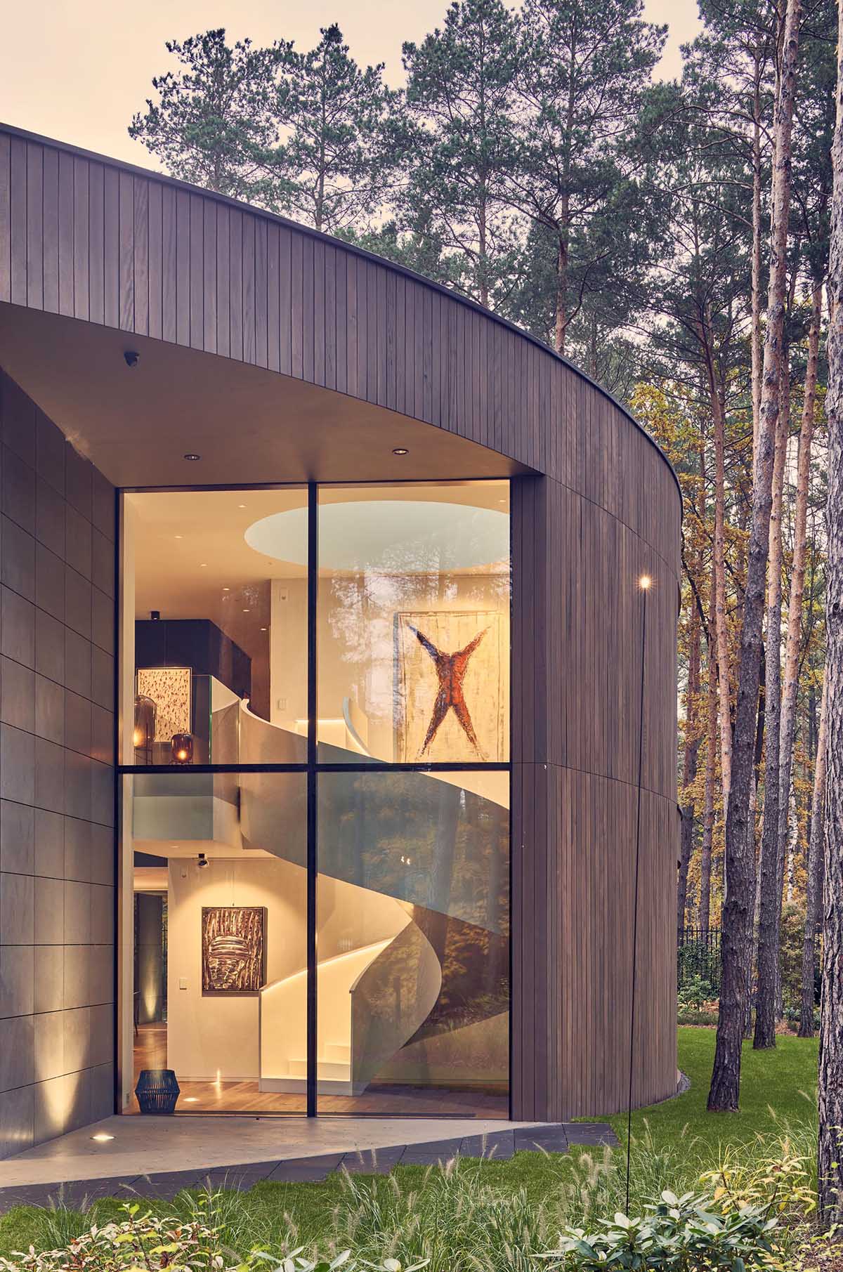 A modern circular home with a wood exterior and large windows that provide a glimpse of the interior.