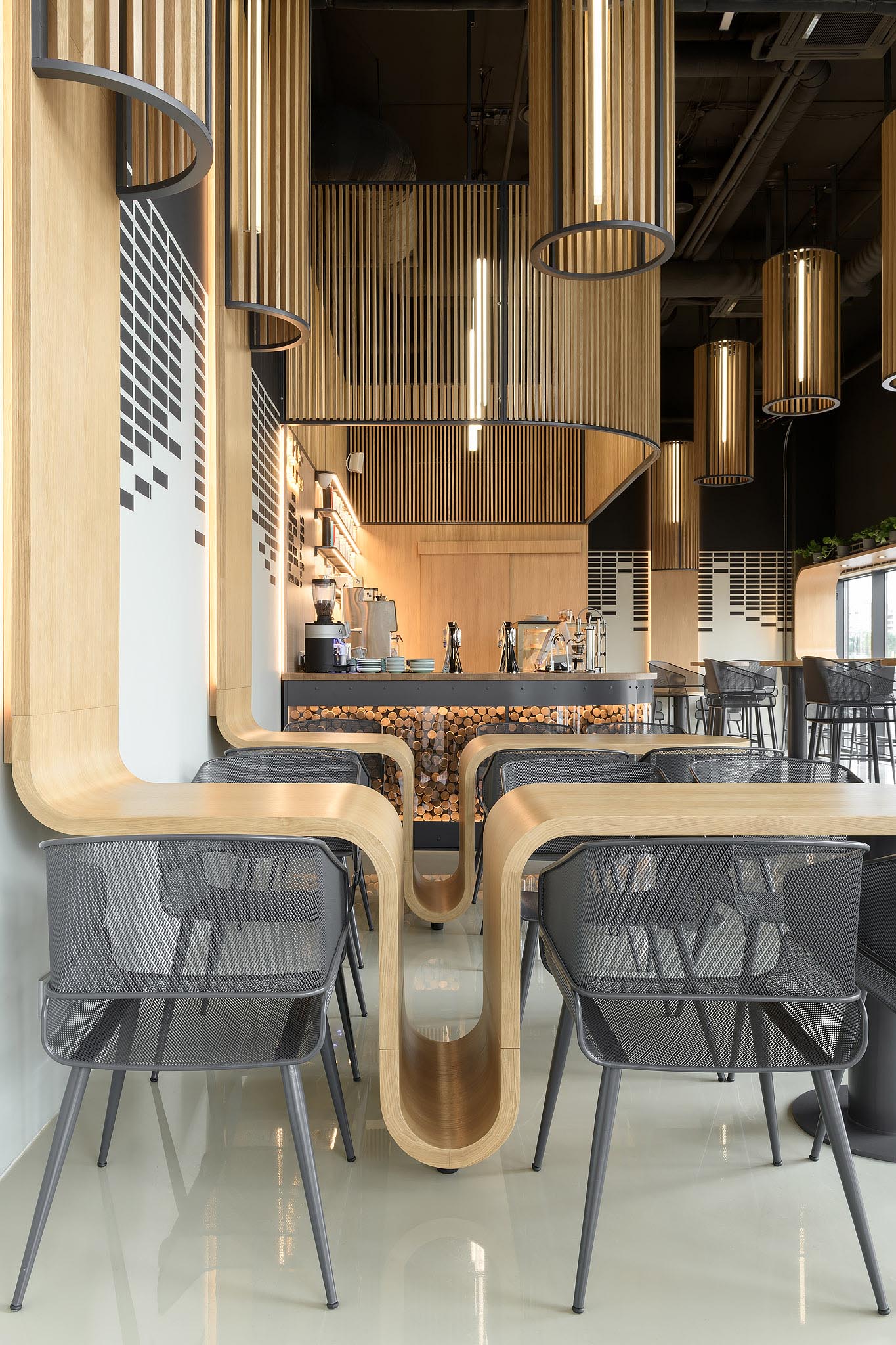 A modern coffee shop with custom designed oak tables that continue onto the wall, and have space for bags to be placed.