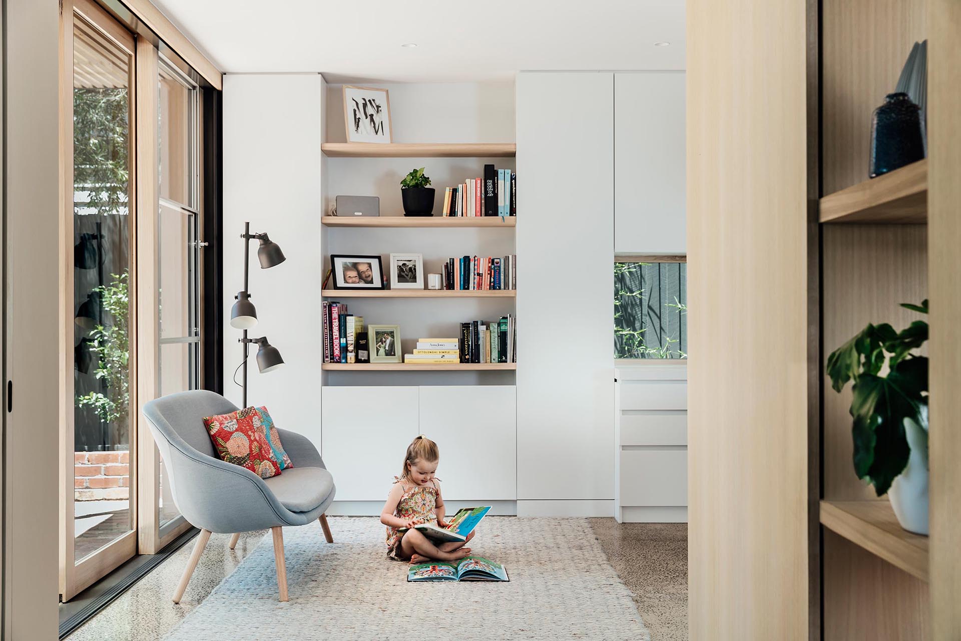 A small reading corner that's furnished with open shelving, a rug, a floor lamp, and a small sofa.