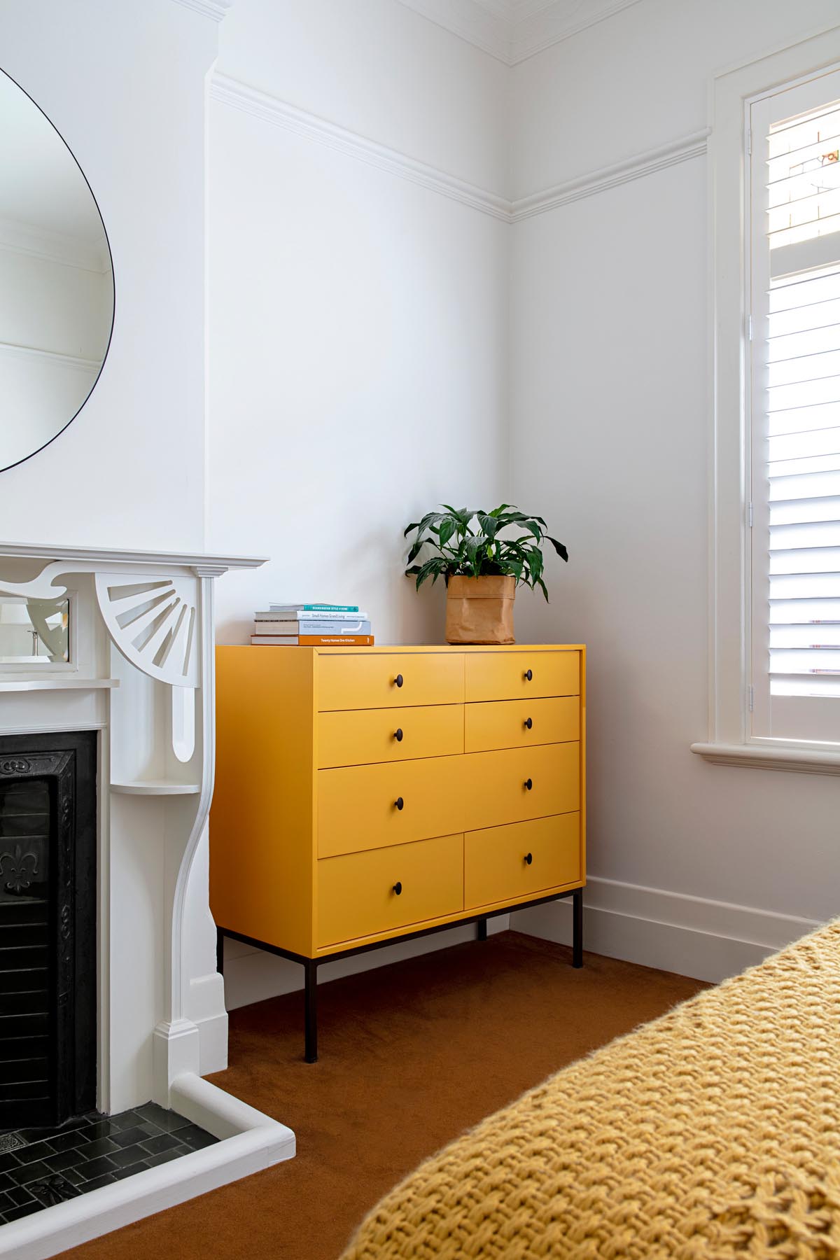 In this updated bedroom, a custom furniture piece in mustard yellow adds a colorful accent that complements both the flooring and bedspread.