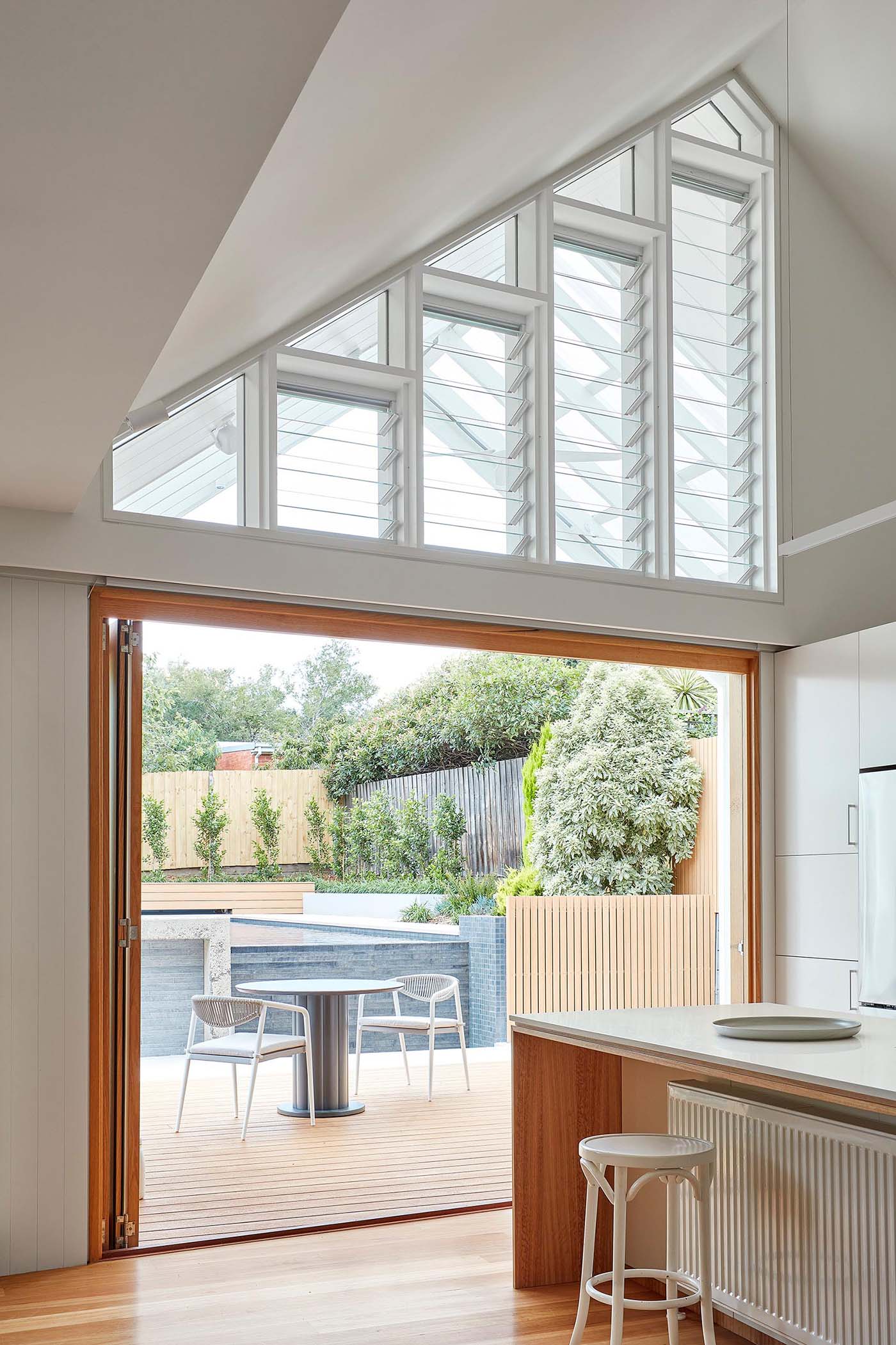 Adjacent to this modern kitchen are folding glass doors that open to a space for outdoor dining, while above, louver windows help with the air flow.