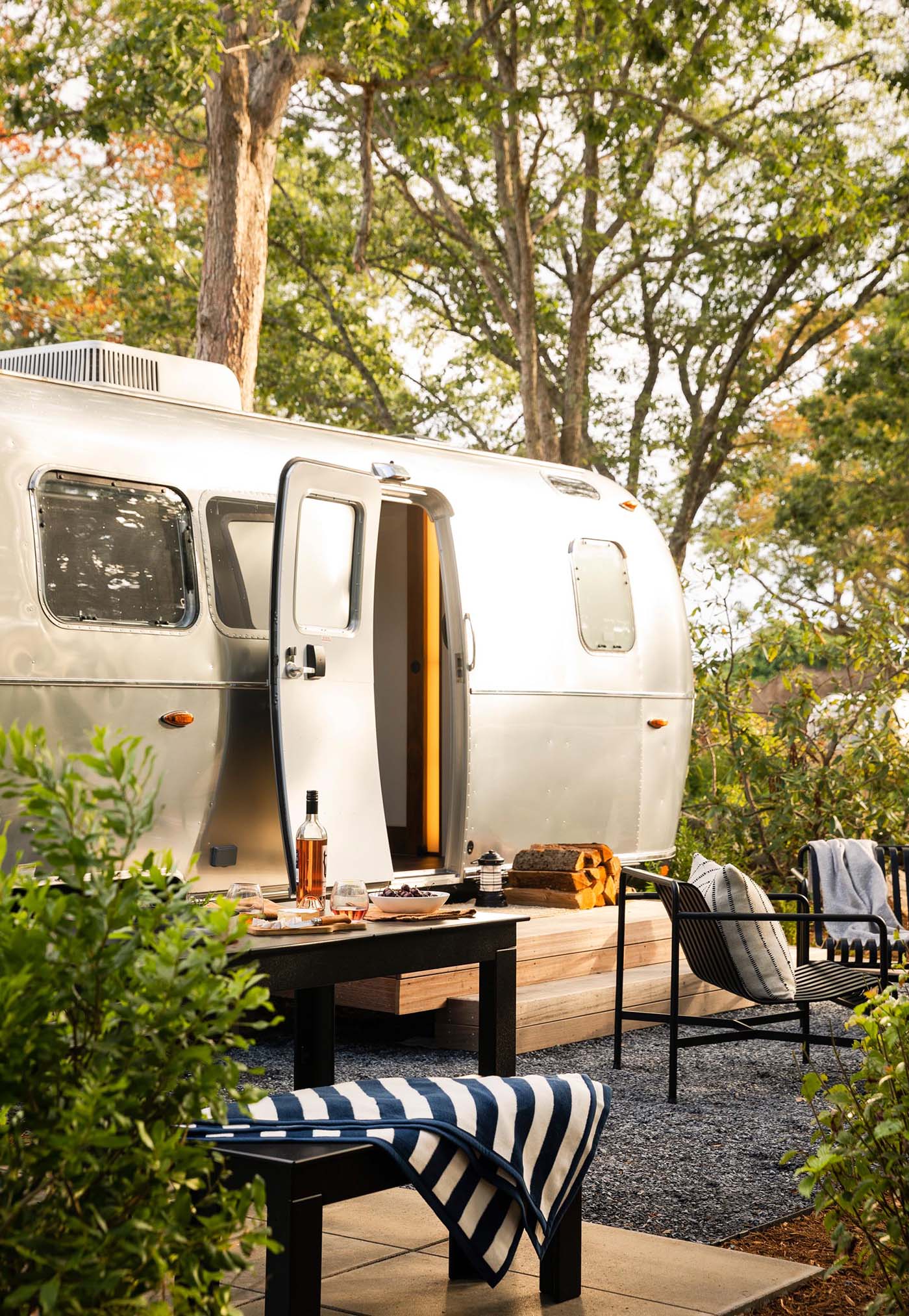 A remodeled Airstream trailer with a dedicated space for outdoor dining, and a small fire pit with a couple of chairs.