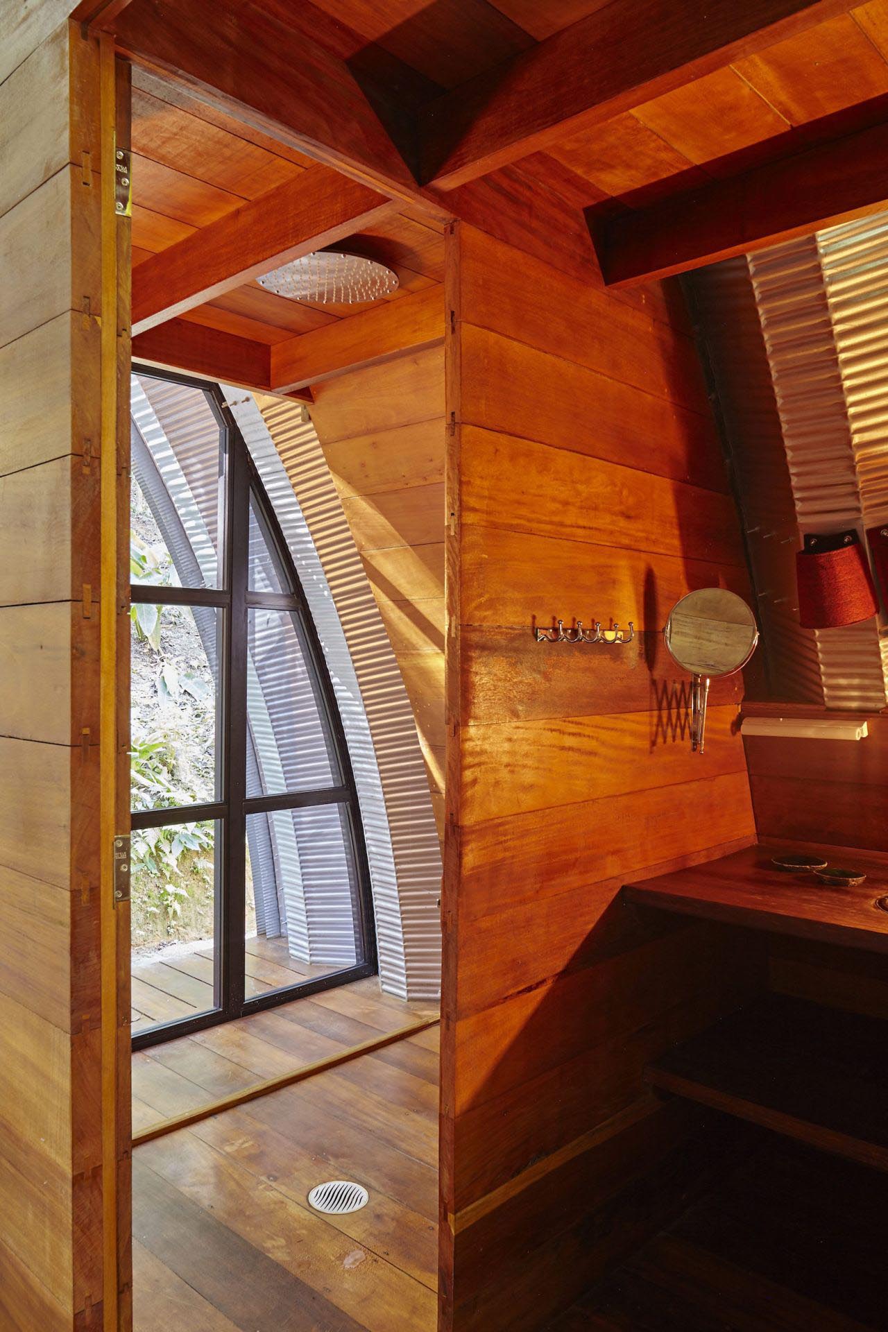 A modern bathroom lined with wood, that has a shower with tree views.