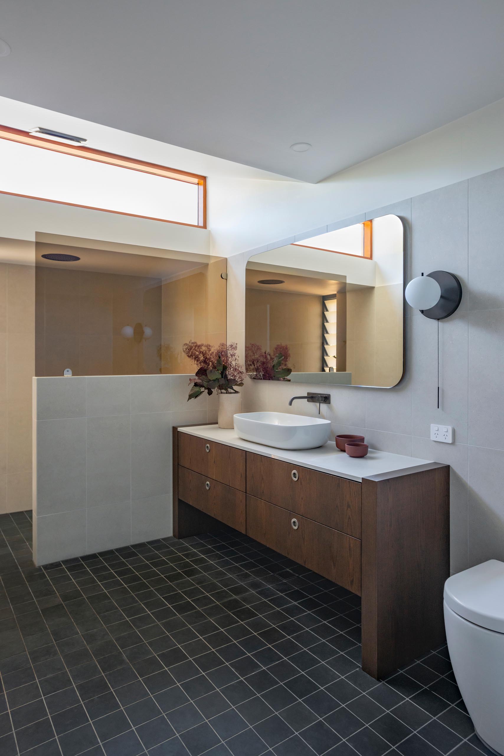 A modern bathroom with a dark wood vanity that's been paired with dark flooring and light colored walls.