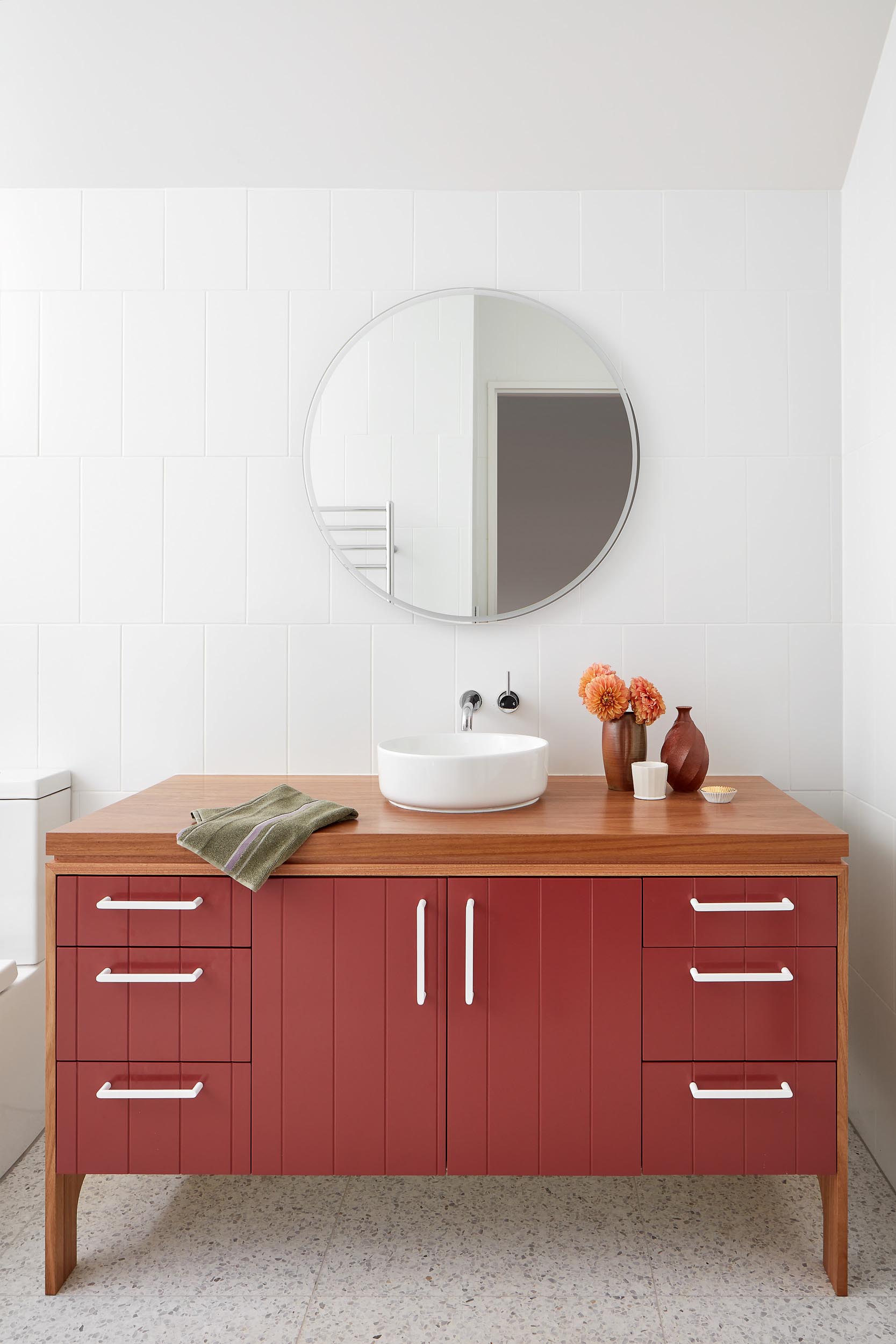 In this modern bathroom, the color for the room comes from the vanity that sits below a round mirror. 