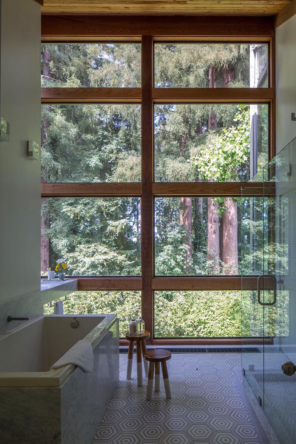 A modern bathroom with a high ceiling and a wall of wood-framed windows.