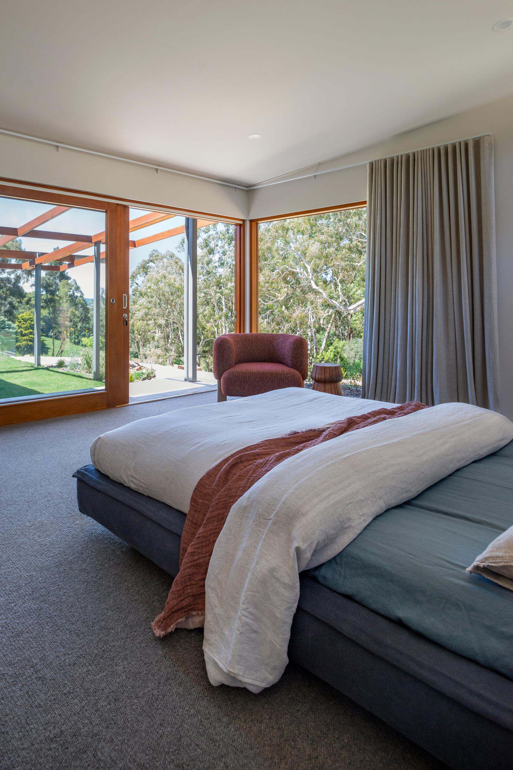 Large windows and a sliding door provide an uninterrupted tree view in a modern bedroom.