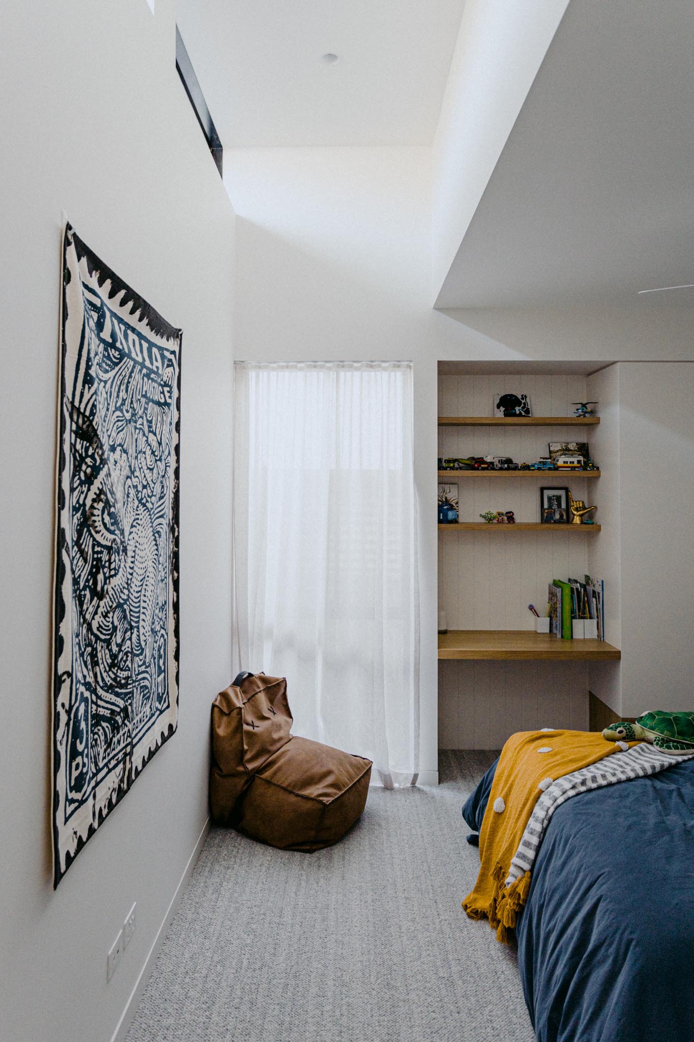 In this modern bedroom, wood shelving and a desk have been built into the wall, while the window adds natural light to the room.