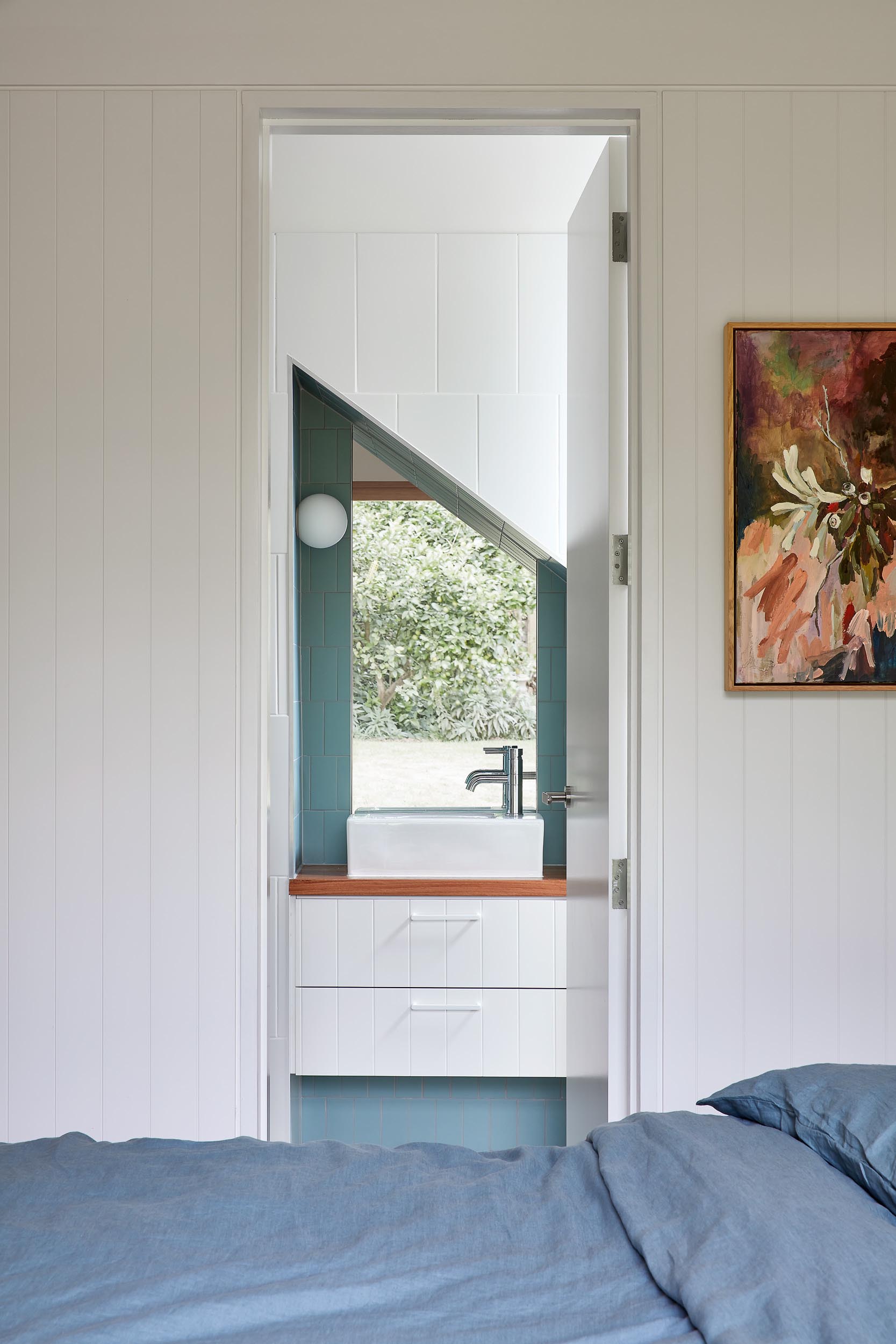 A modern bedroom has an en-suite bathroom with an angled mirror.