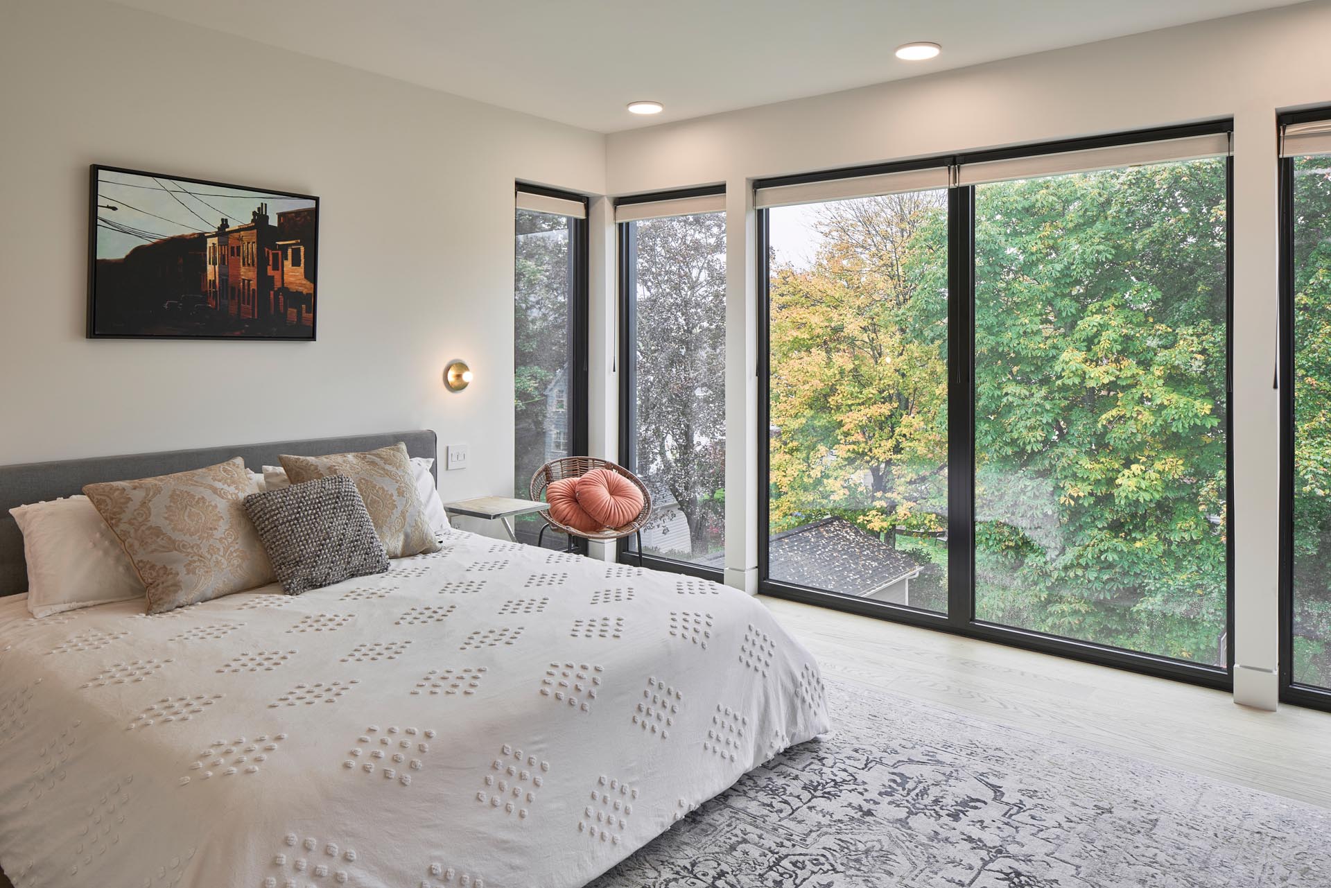 A modern bedroom with large black-framed windows that showcase the greenery outside.