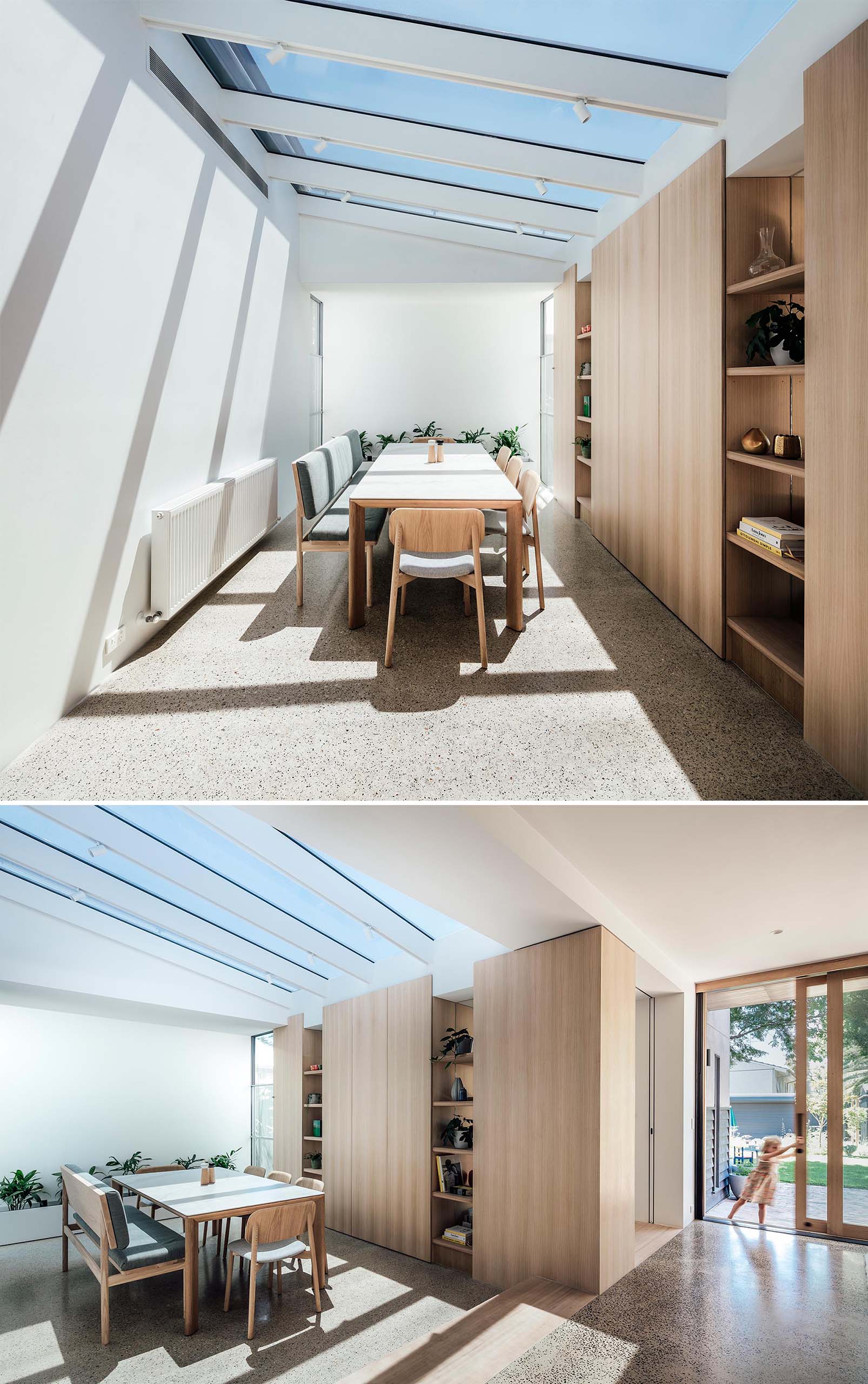 In this modern dining room, multiple skylights flood the room with natural light, while at the same time, create shadows along the wall. On the opposite wall, custom joinery creates plenty of storage space, while the table is surrounded by chairs as well as a bench. Polished concrete flooring rounds out the contemporary interior.