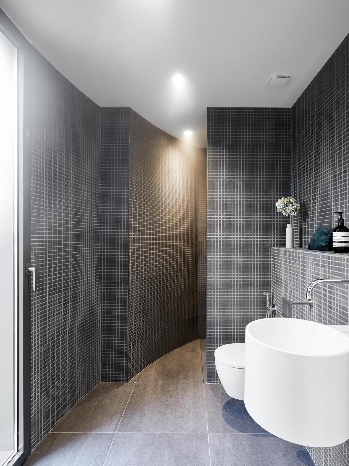 A modern bathroom with walls covered in small square grey tiles.
