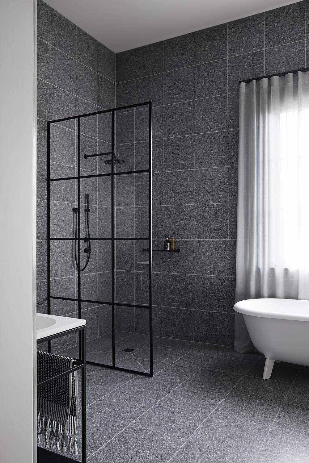 Modern grey and black bathroom with terrazzo tile covered walls, and a black framed glass shower screen.